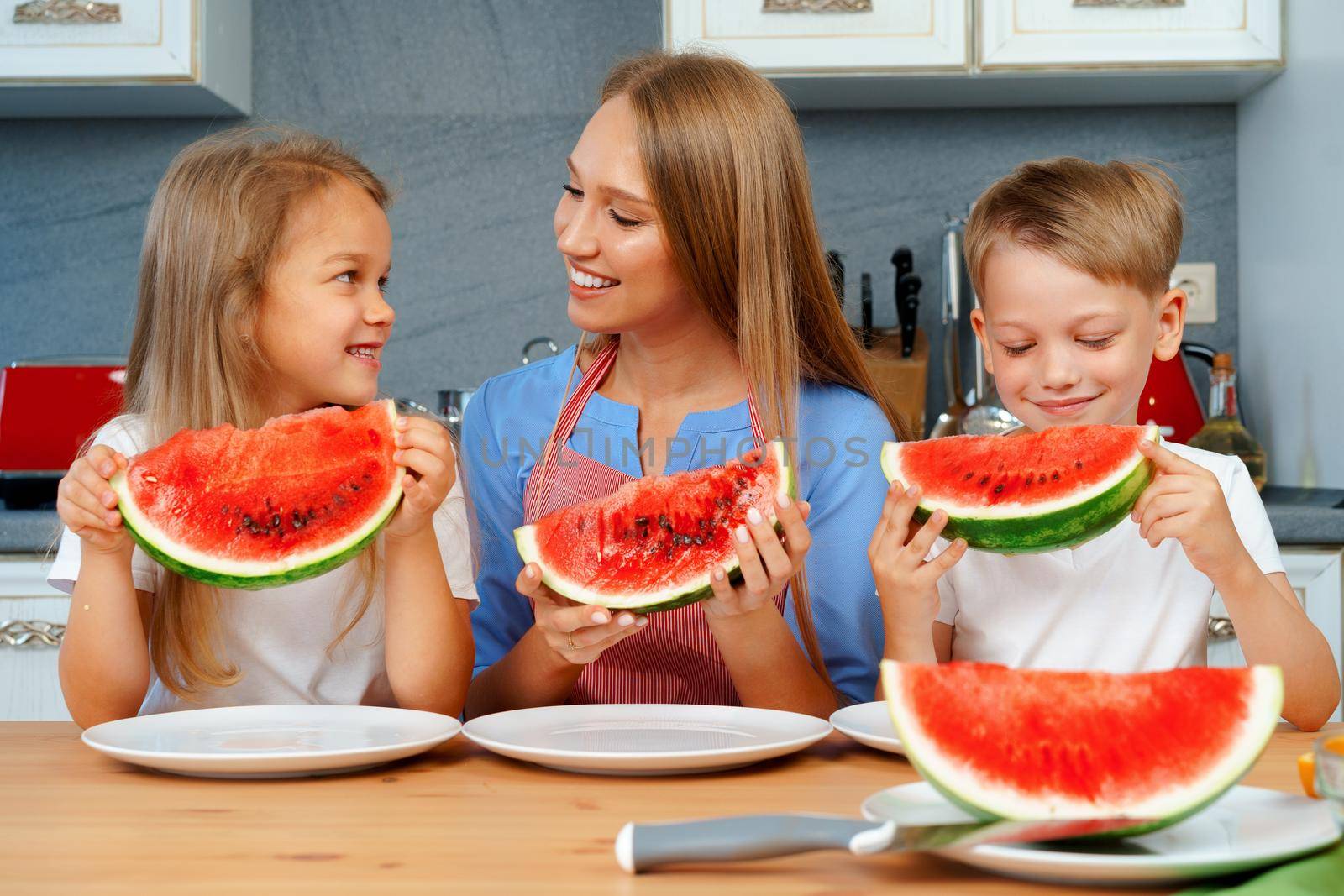 Sweet family, mother and her kids eating watermelon in their kitchen having fun, close up