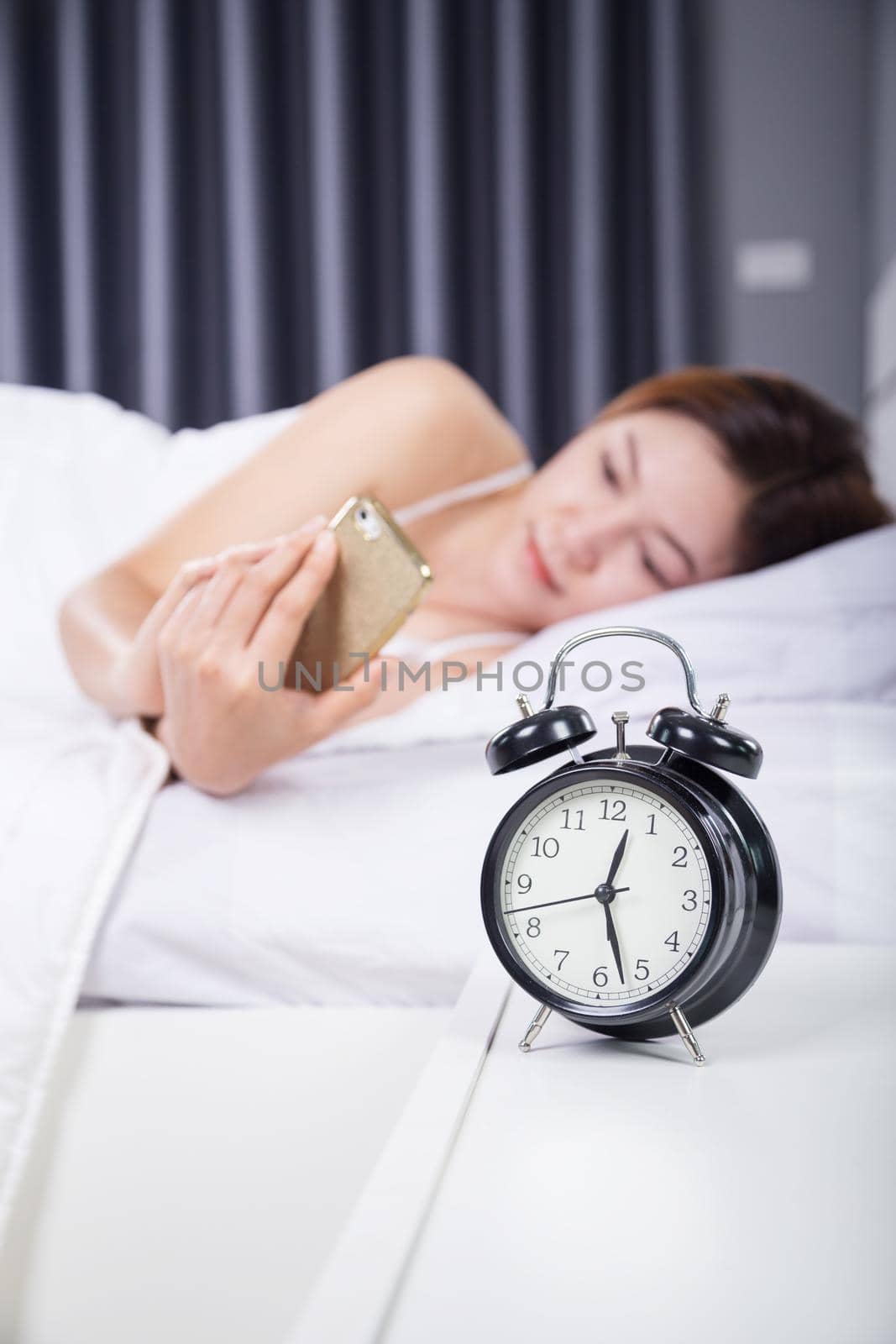 clock with woman using her smartphone on bed in the bedroom 