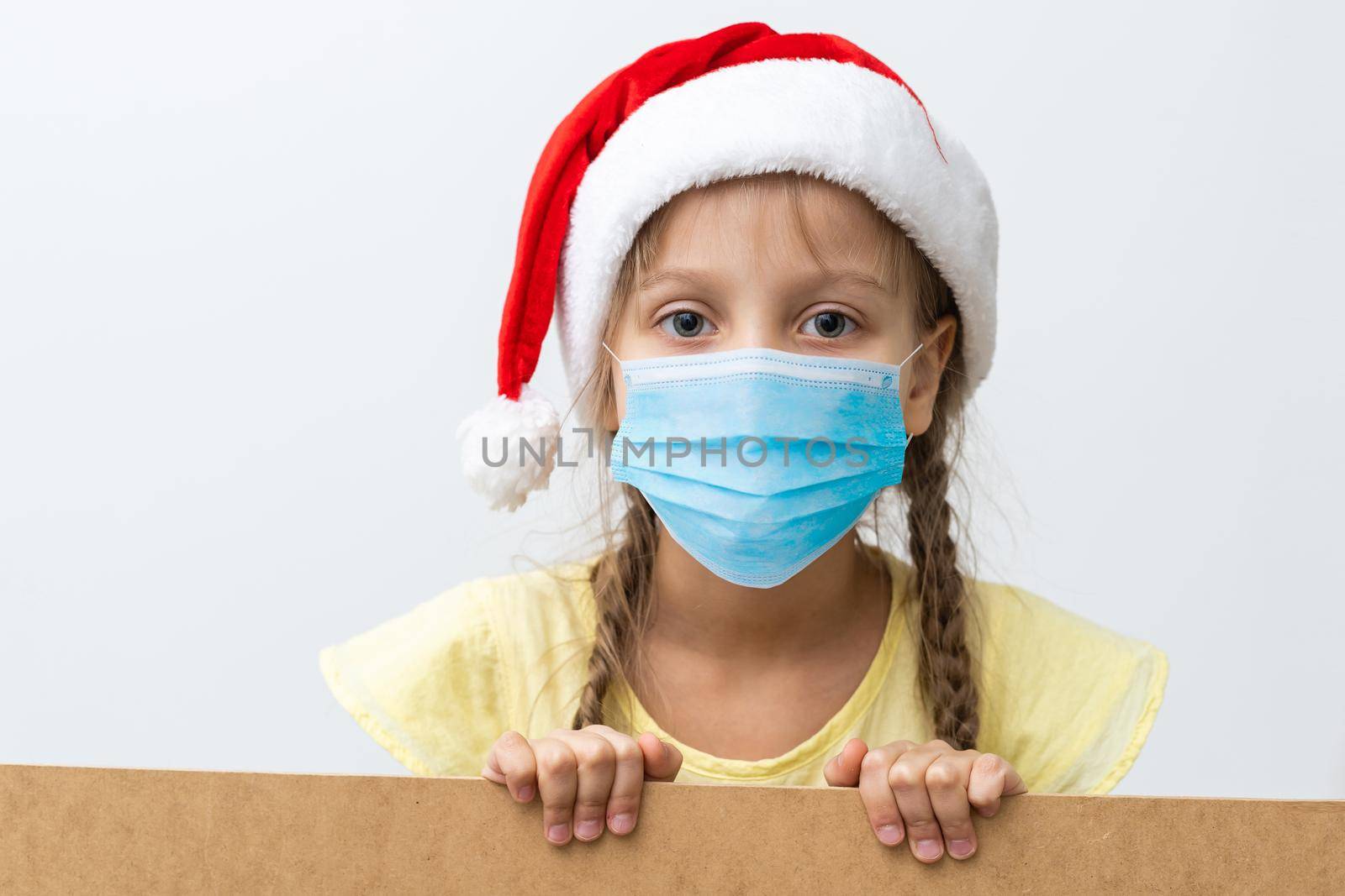 Portrait of a beautiful little girl wearing Santa hat, medical mask, isolated on white background, copy space. celebrating happy New Year. Child safety social distance by Andelov13