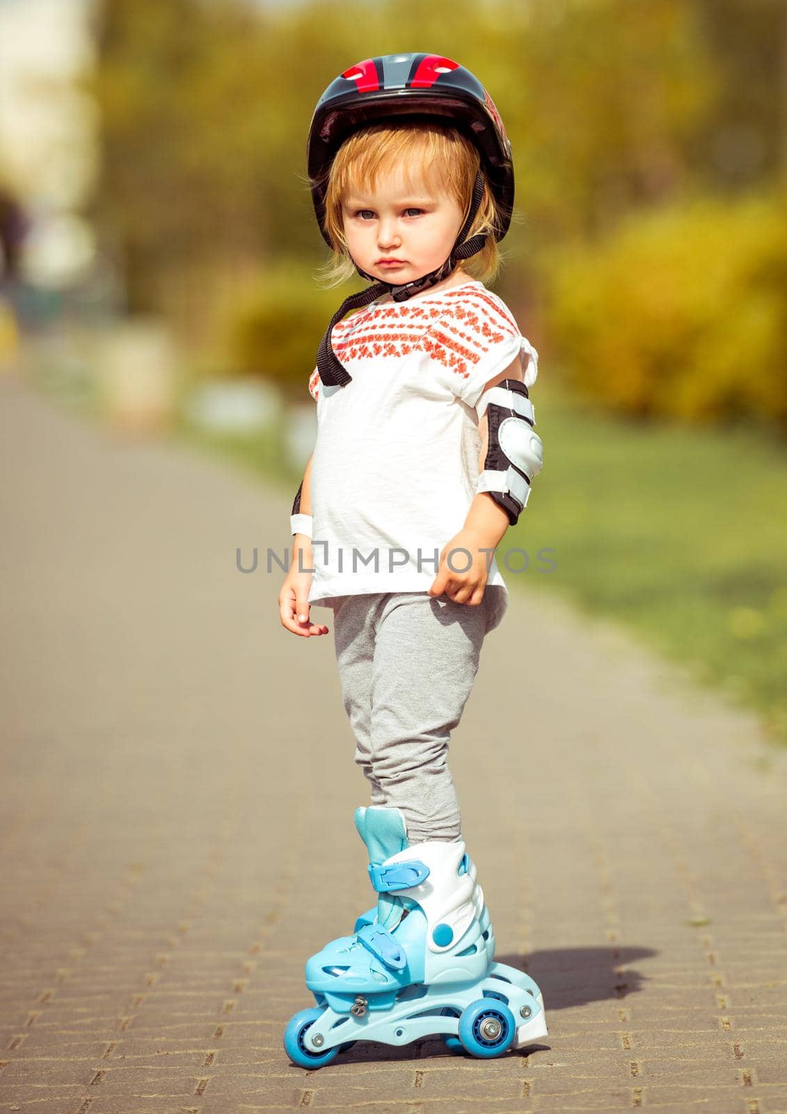 two year old pretty girl in roller skates and a helmet on the street