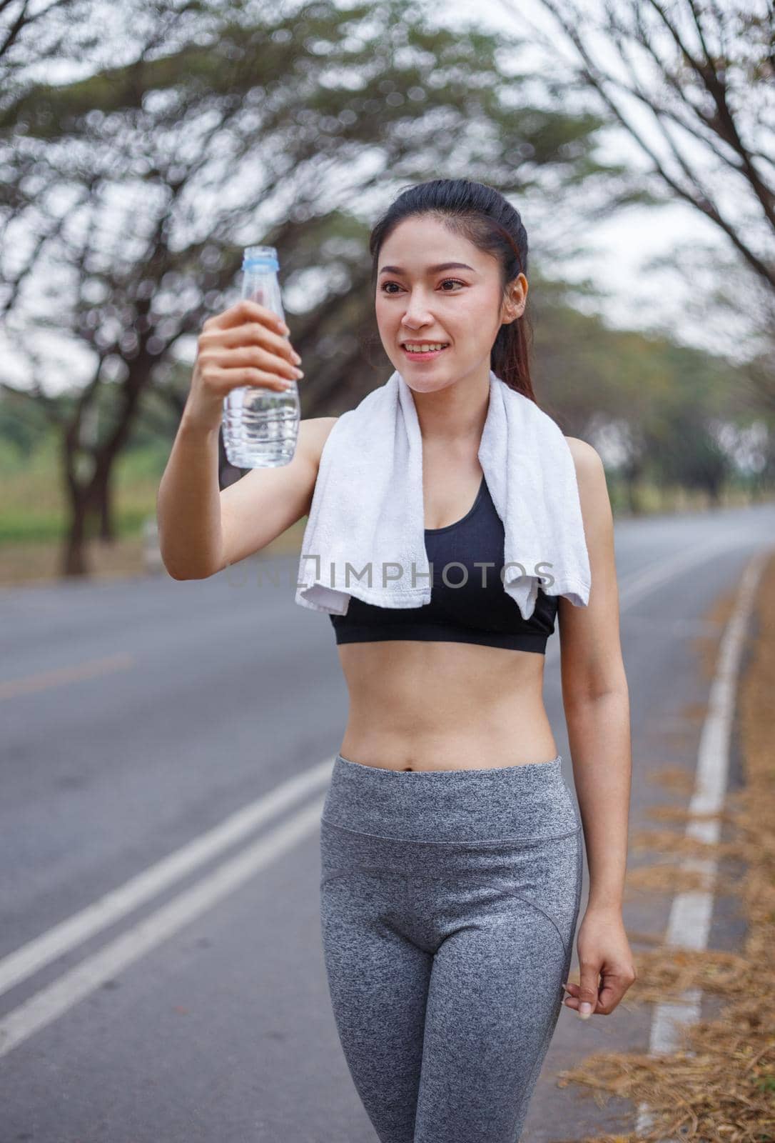 young sporty woman with bottle of water in park by geargodz