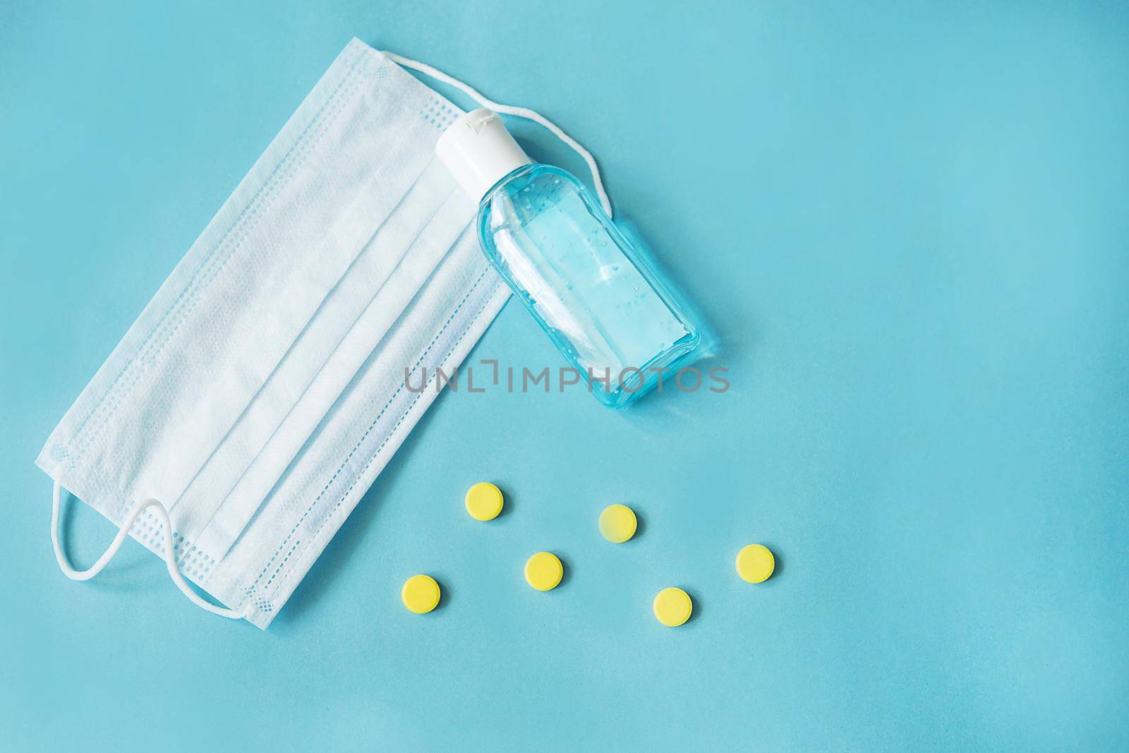Respiratory mask, atibacterial hand treatment and medicine in capsules on blue background.Virus prevention and treatment.
