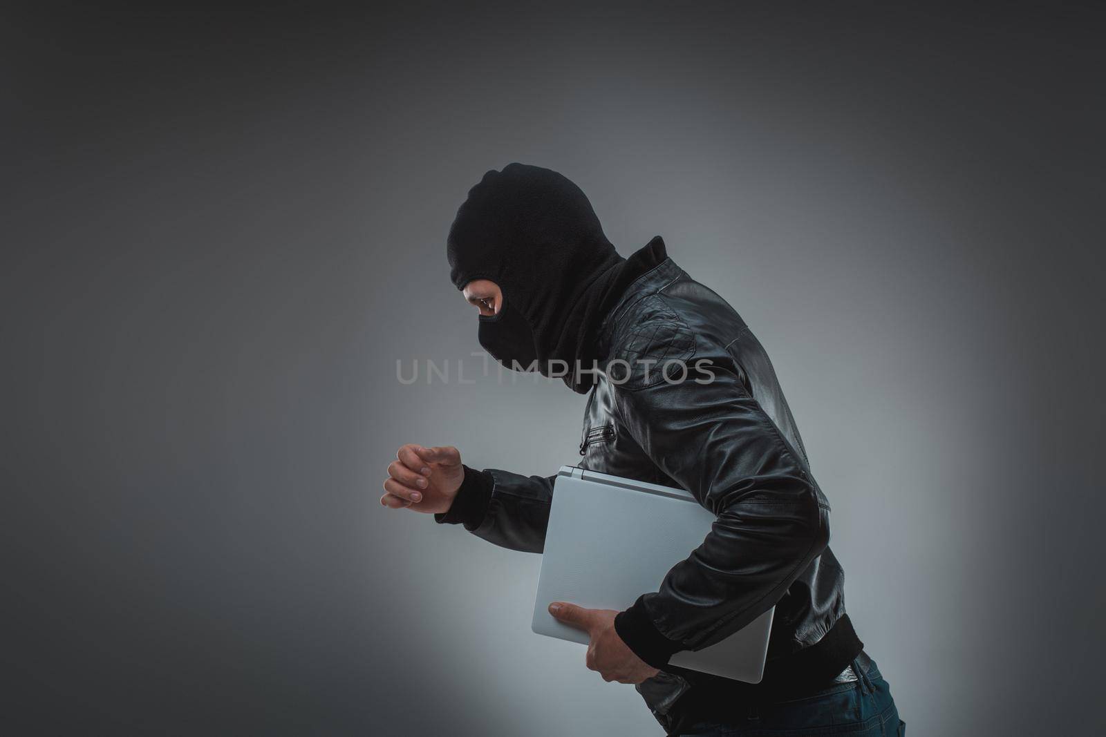 Thief stealing a laptop computer. Isolated on gray background. Studio shot