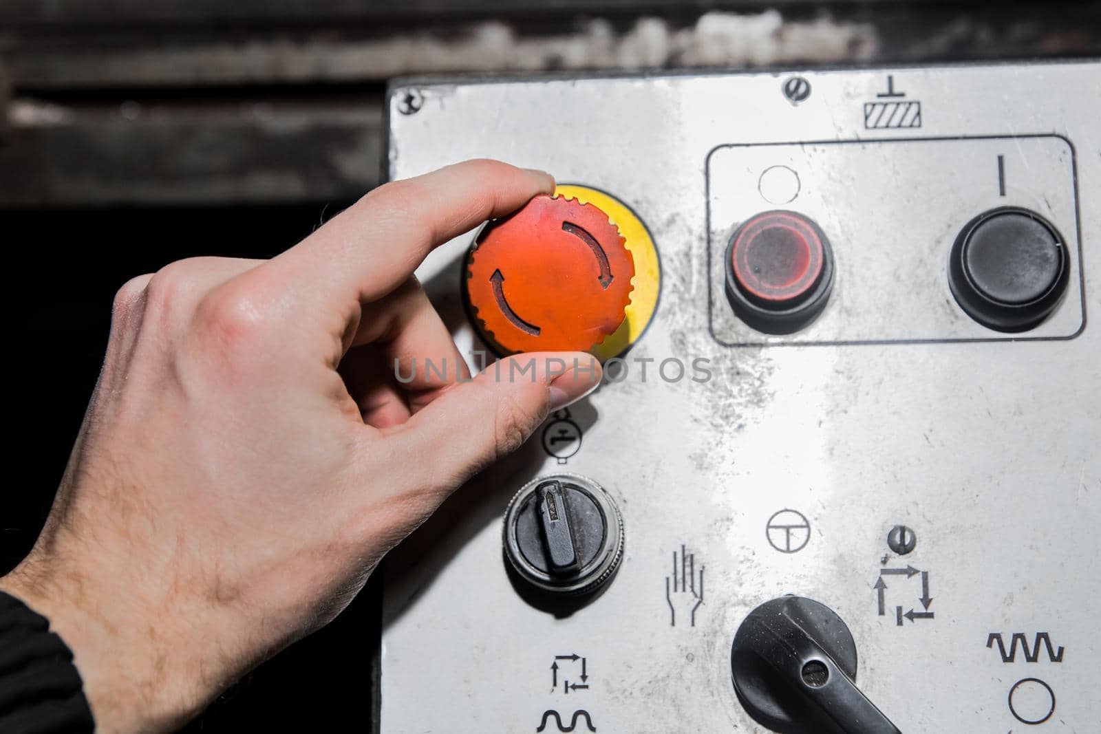 A man's hand turns the red button on an old industrial equipment control system.