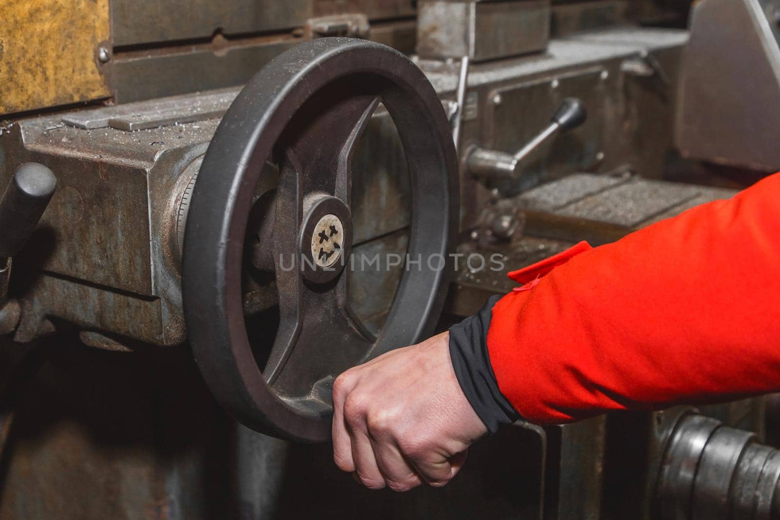 The hand of a man worker holds a special, steering wheel by the handle and controls the work of the milling machine in an industrial plant.