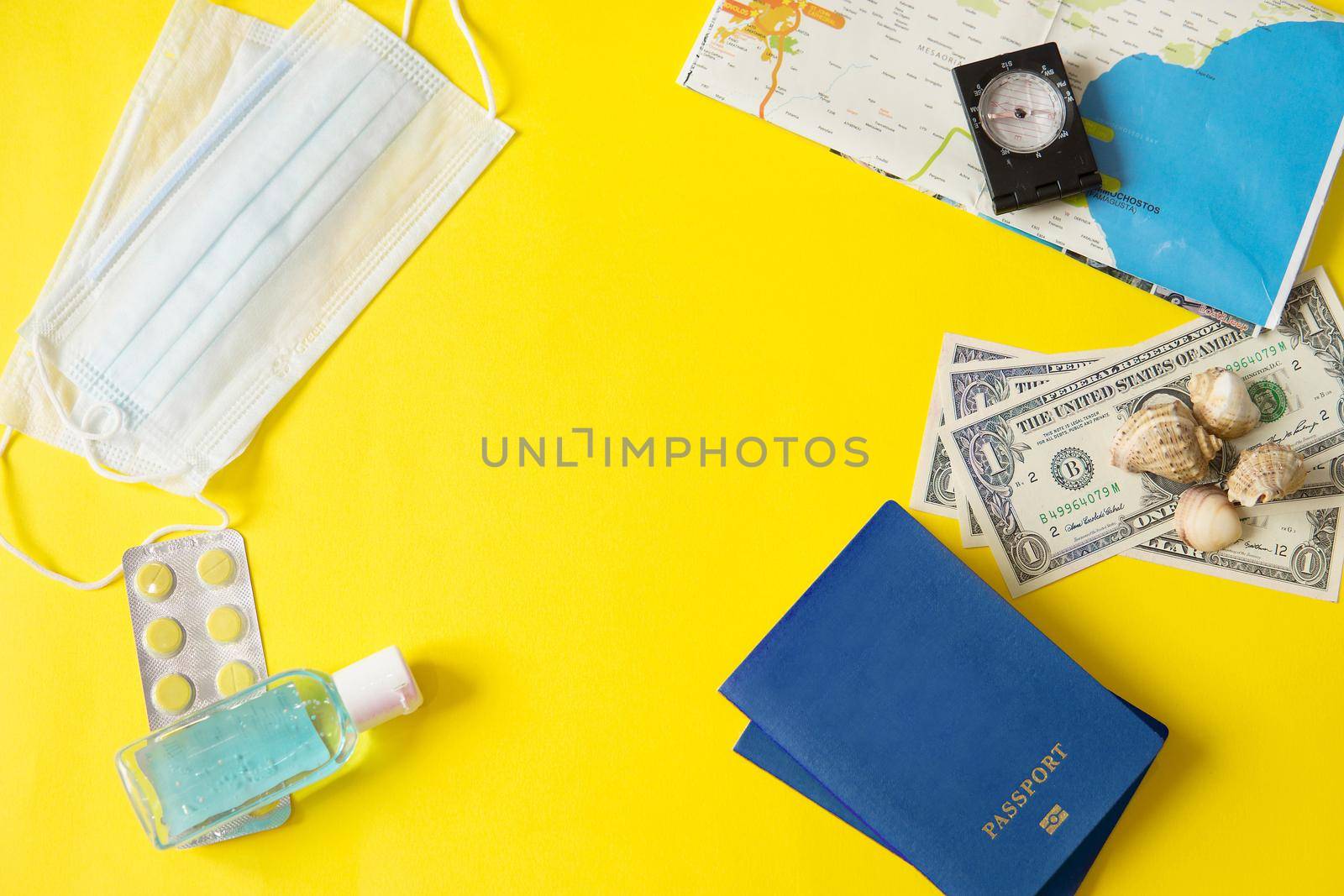 Travel concept with tablets, sterile mask, antiseptic and road symbols id passport, money, compass, map on yellow background. Stop traveling to dangerous places to prevent coronavirus. Space for text