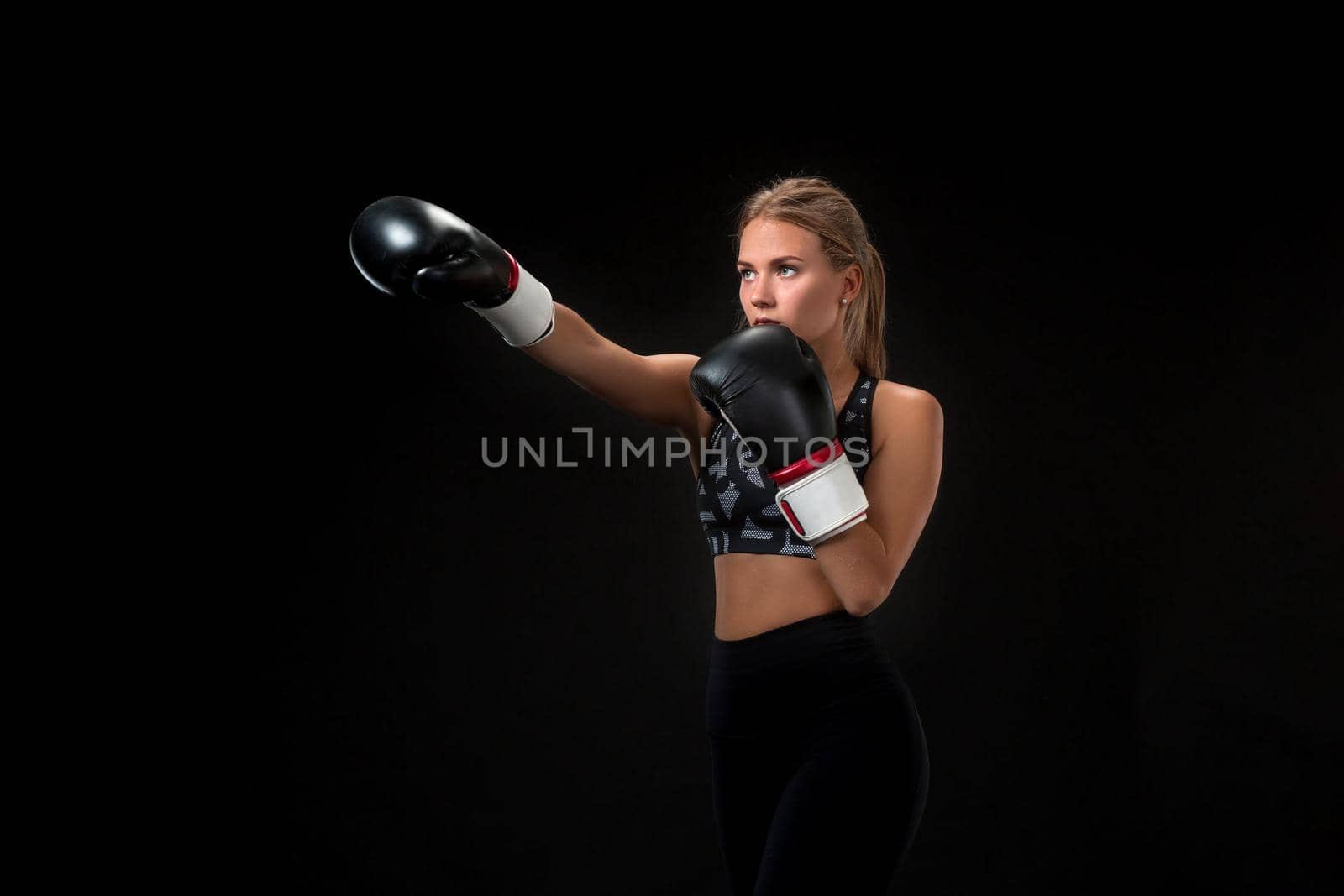 Beautiful female athlete in boxing gloves, in the studio on a black background. The boxer fulfills the blow