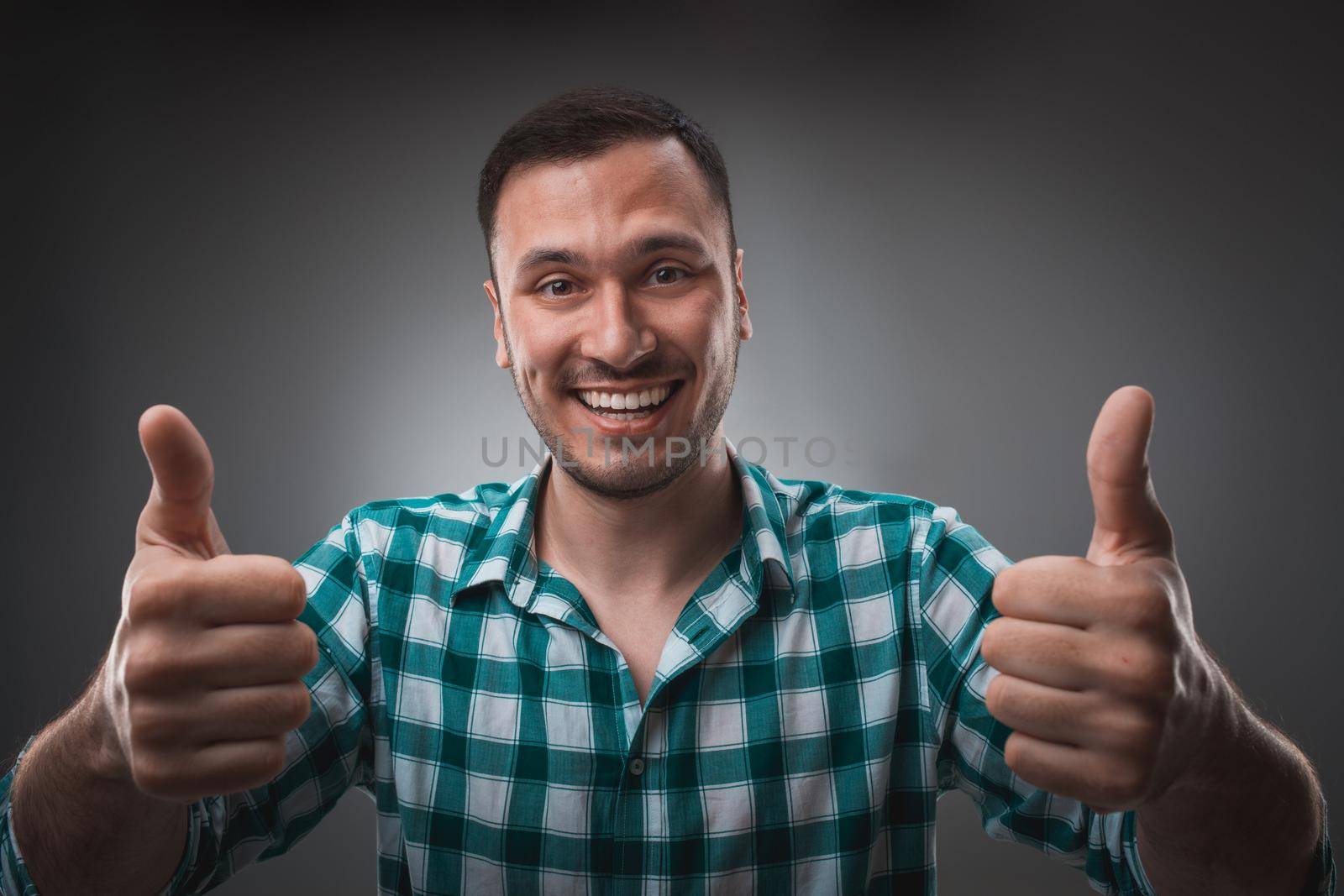 Portrait of excited happy man showing thumb up sign and smiling. Isolated on gray background. Emotion concept