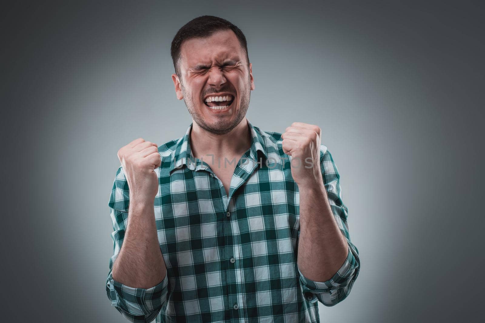 Young man and sign of victory isolated on gray background. Emotion concept