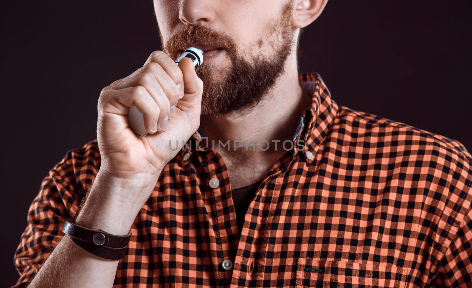 young man wearing a plaid shirt smokes an electronic cigarette on a black background. close-up