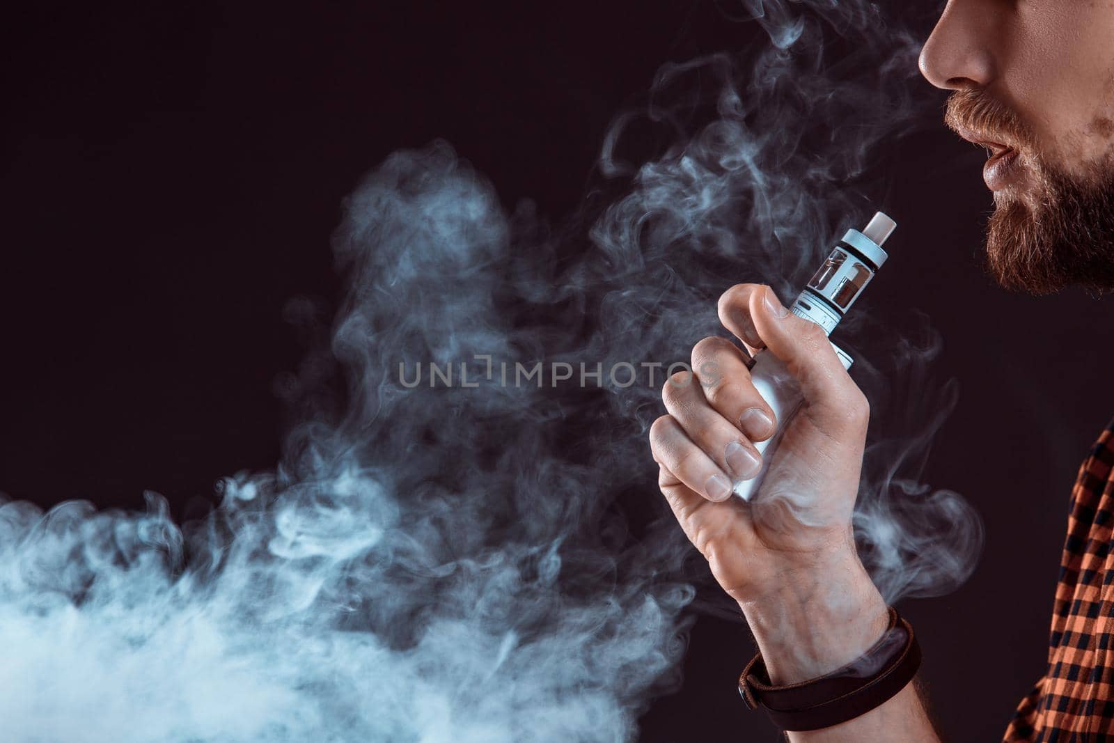 young man wearing a plaid shirt smokes an electronic cigarette on a black background. close-up