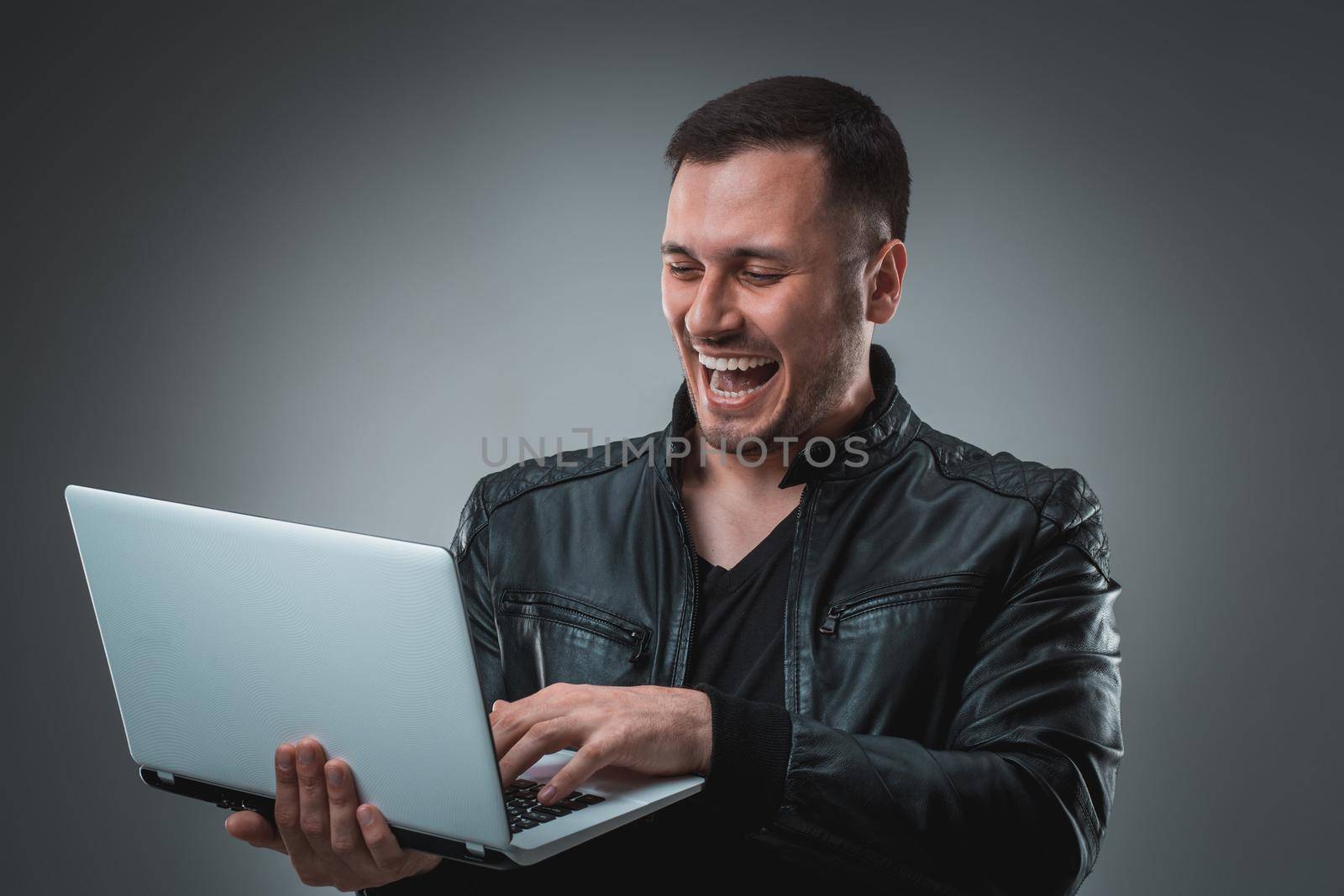 Happy man holding laptop on gray background. Portrait of a man in a black jacket in the studio