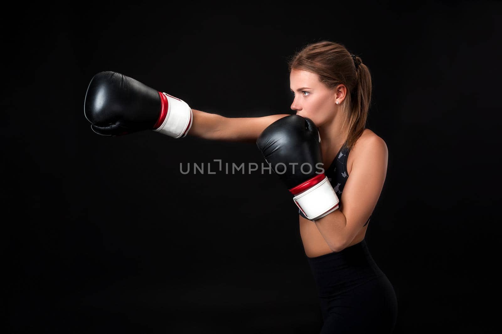 Beautiful female athlete in boxing gloves, in the studio on a black background. The boxer fulfills the blow