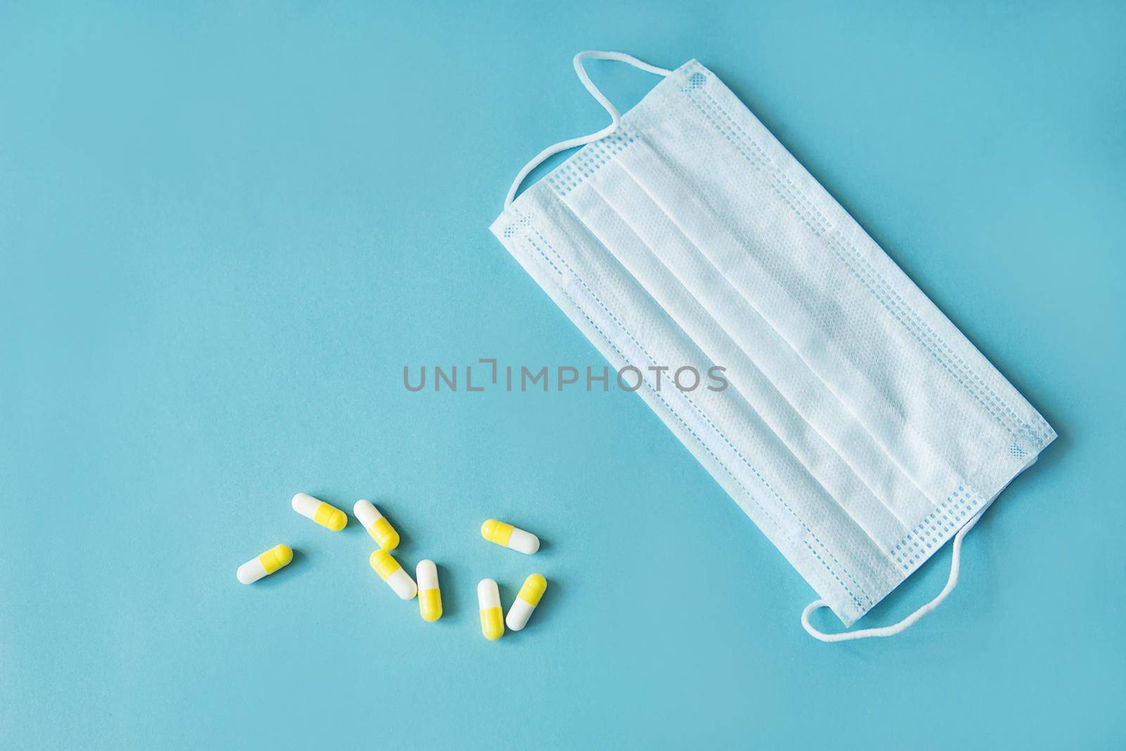 Respiratory mask and medicine in capsules on blue background.Virus prevention and treatment.
