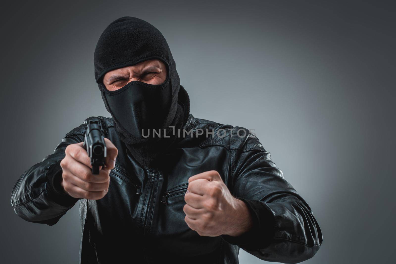 Burglar or terrorist in black mask shooting with gun. A man in the studio on a black-and-gray background