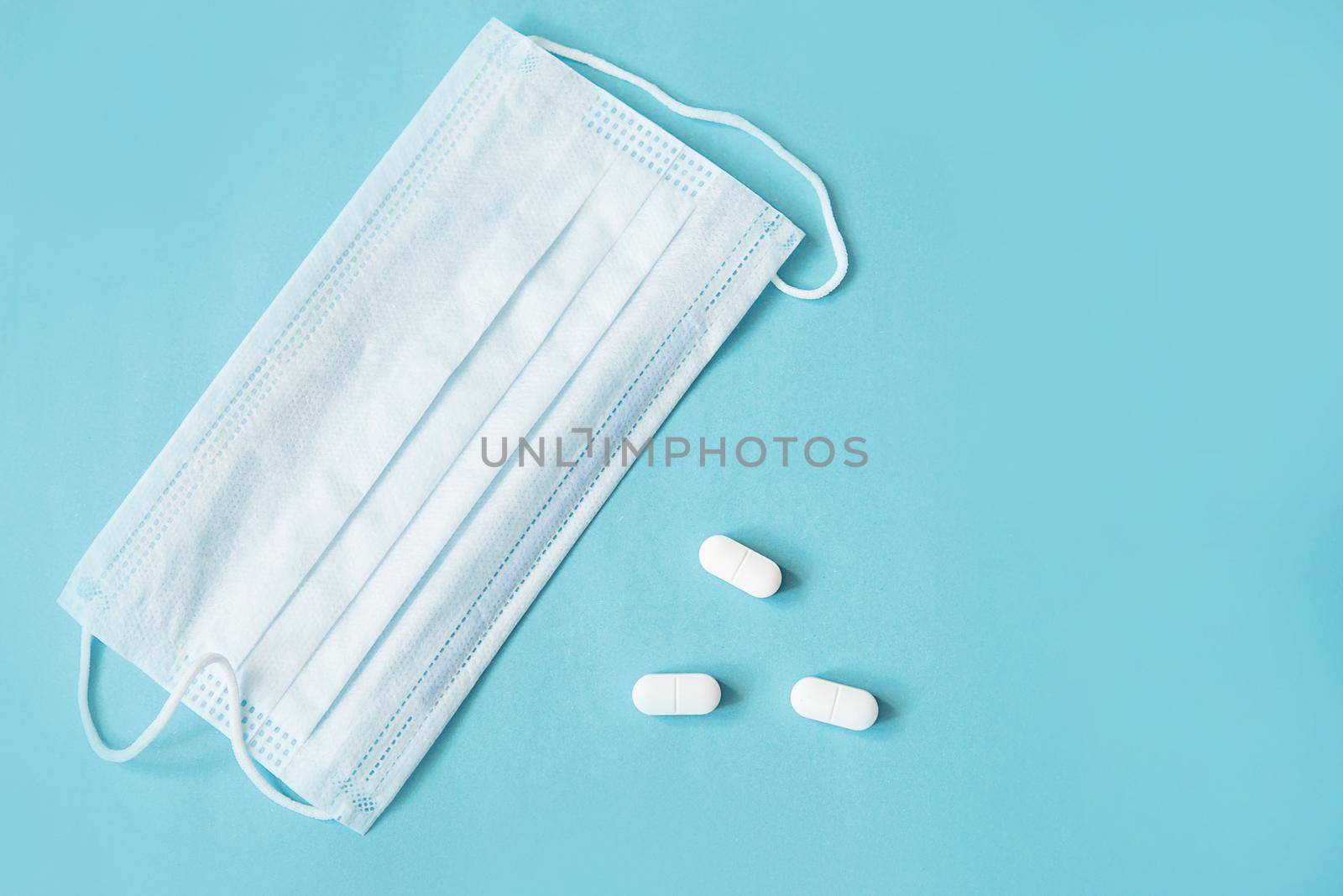 Respiratory mask and medicine in capsules on blue background.Virus prevention and treatment.