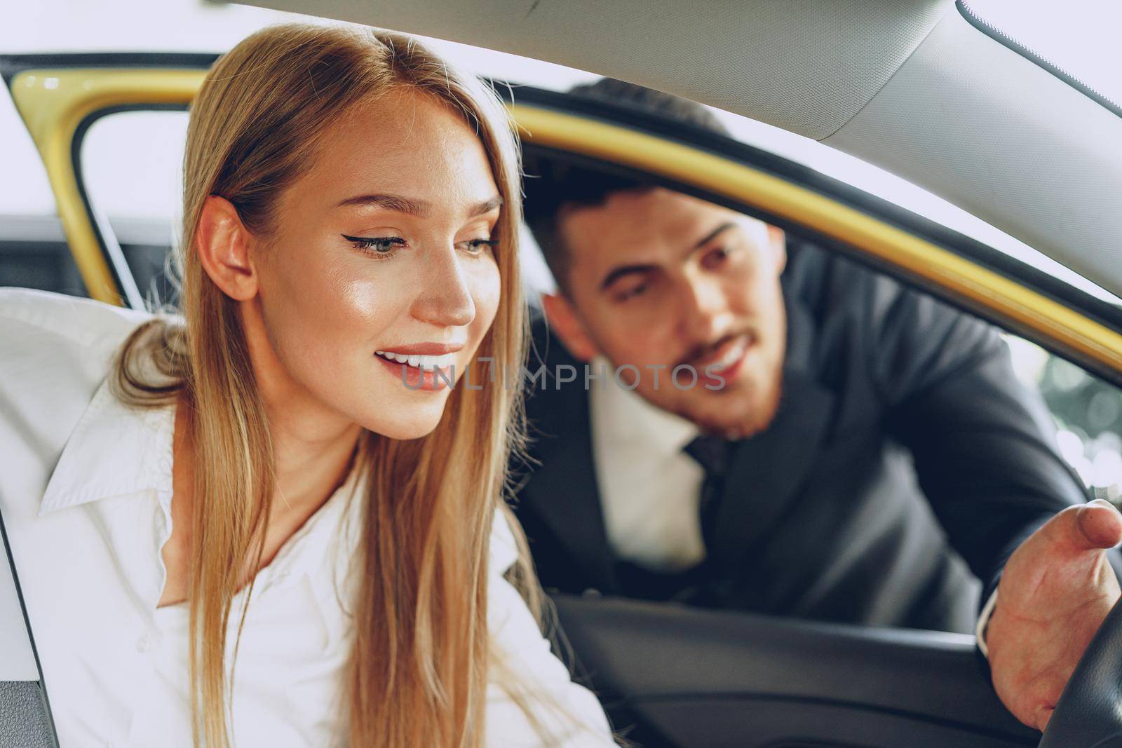 Man car dealer showing a woman buyer a new car in car salon