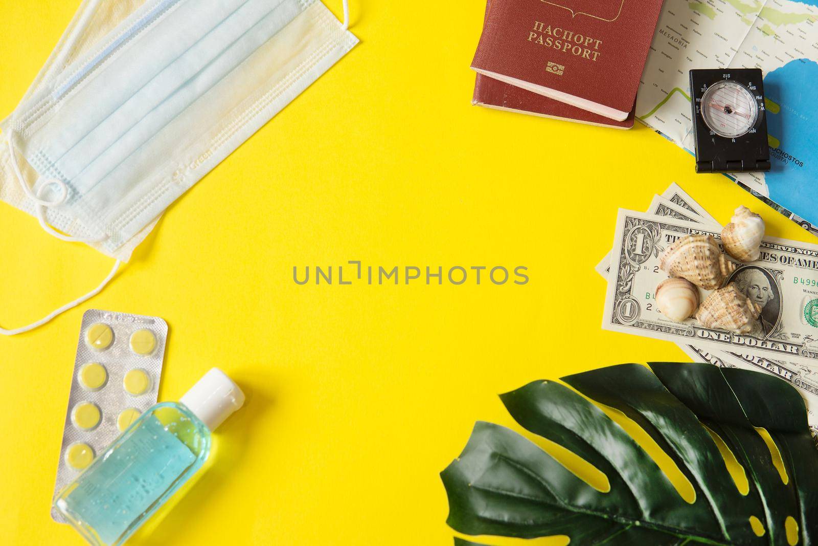 Travel concept with tablets, sterile mask, antiseptic and road symbols id passport, money, compass, map on yellow background. Stop traveling to dangerous places to prevent coronavirus. Space for text