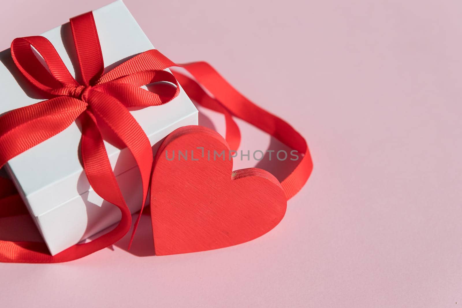 Gift box with red bow ribbon and empty paper note on wooden table for Valentines day