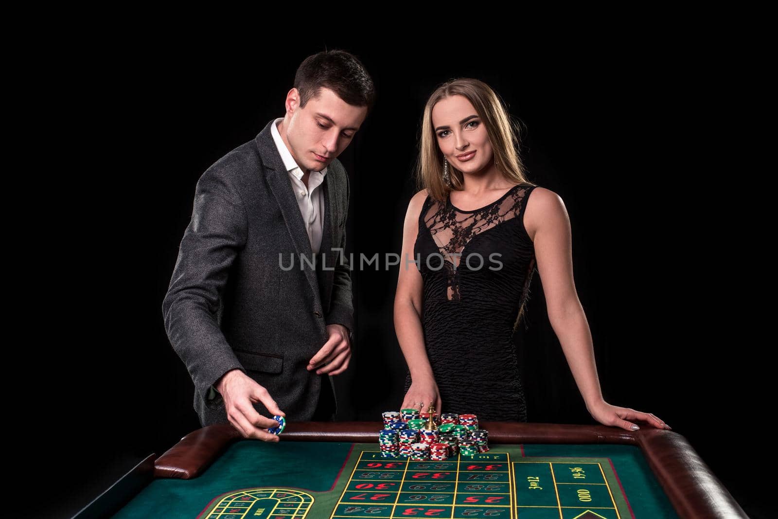 Elegant couple at the casino betting on the roulette, on a black background. A man in a suit with a beautiful young woman in a black dress