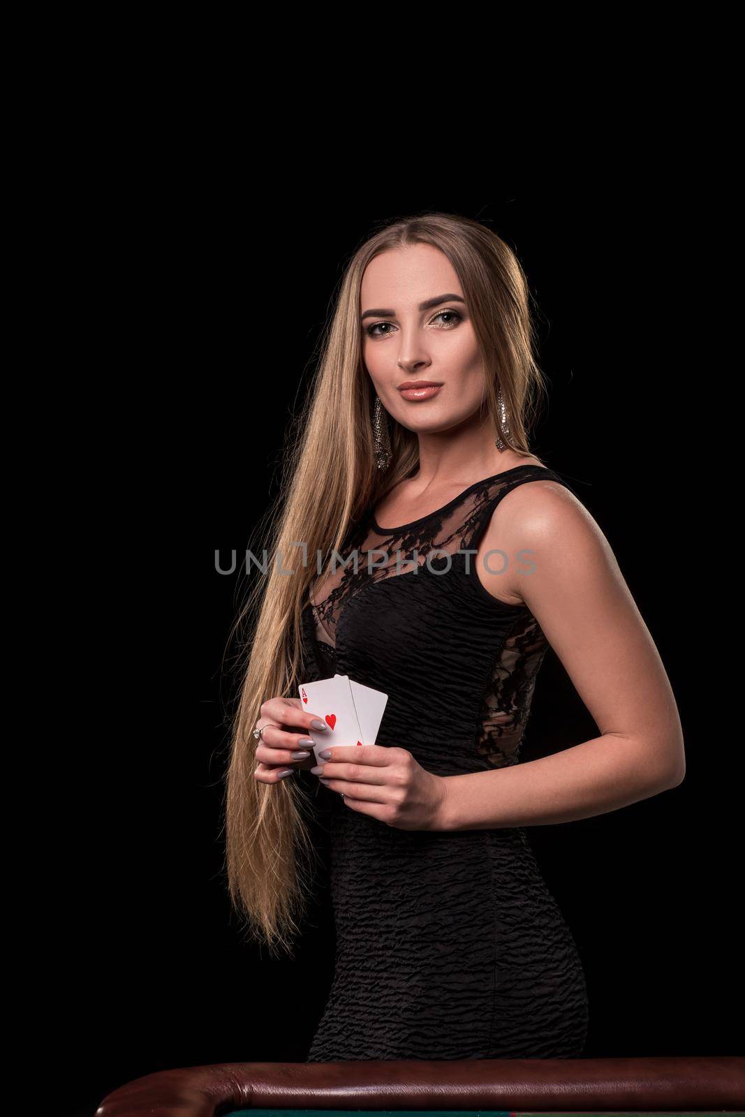 Young beautiful woman in a sexy black dress playing in casino. Girl holding the winning combination of poker cards on a black background. Two aces