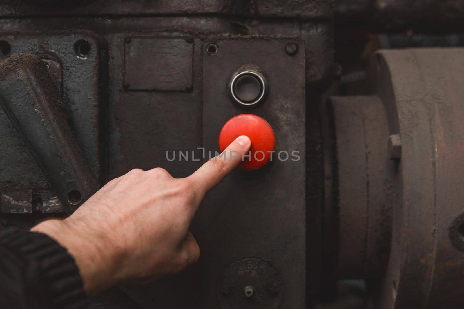 The worker's hand presses the red button on the old system of industrial equipment with his finger.