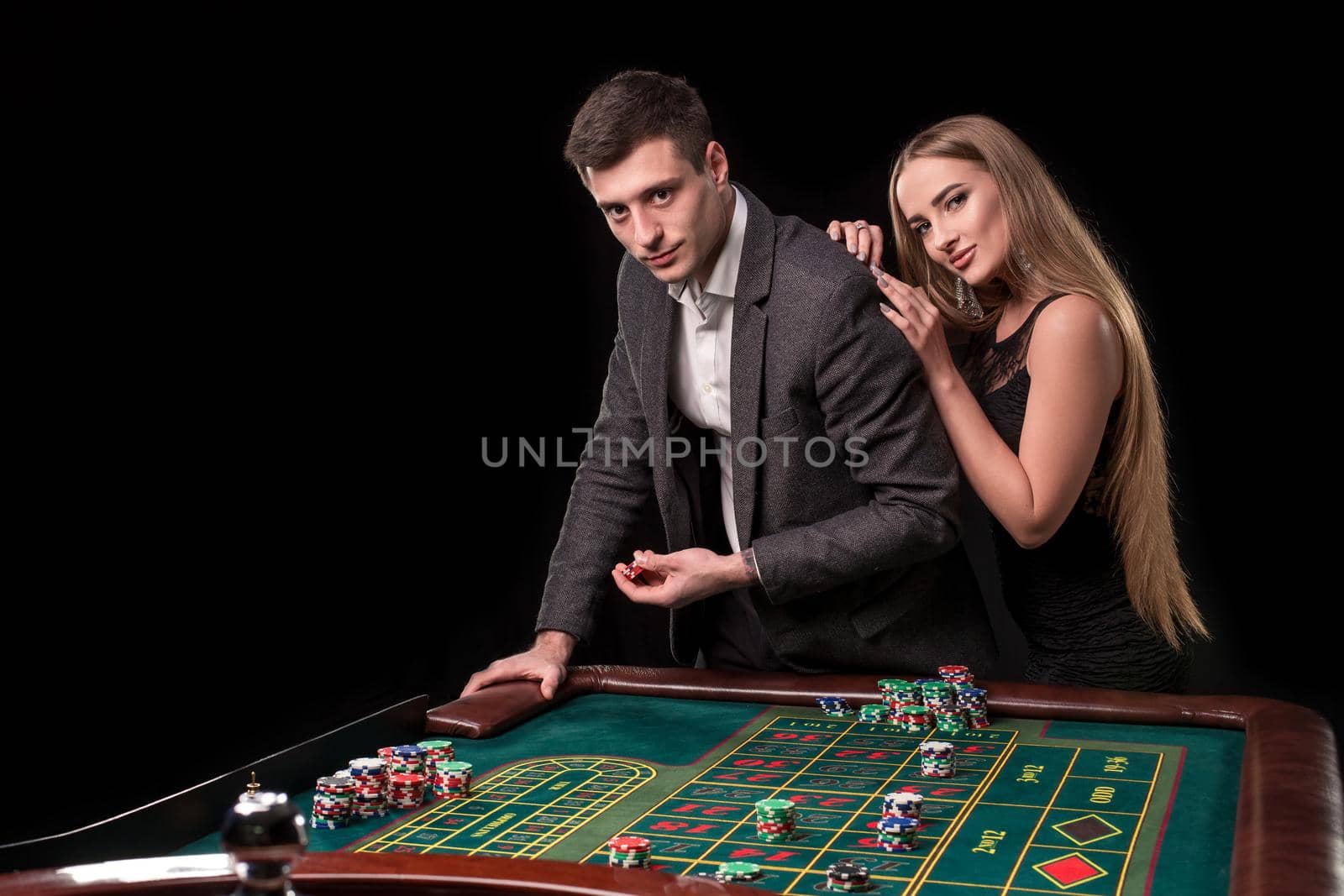 Elegant couple at the casino betting on the roulette, on a black background. A man in a suit with a beautiful young woman in a black dress