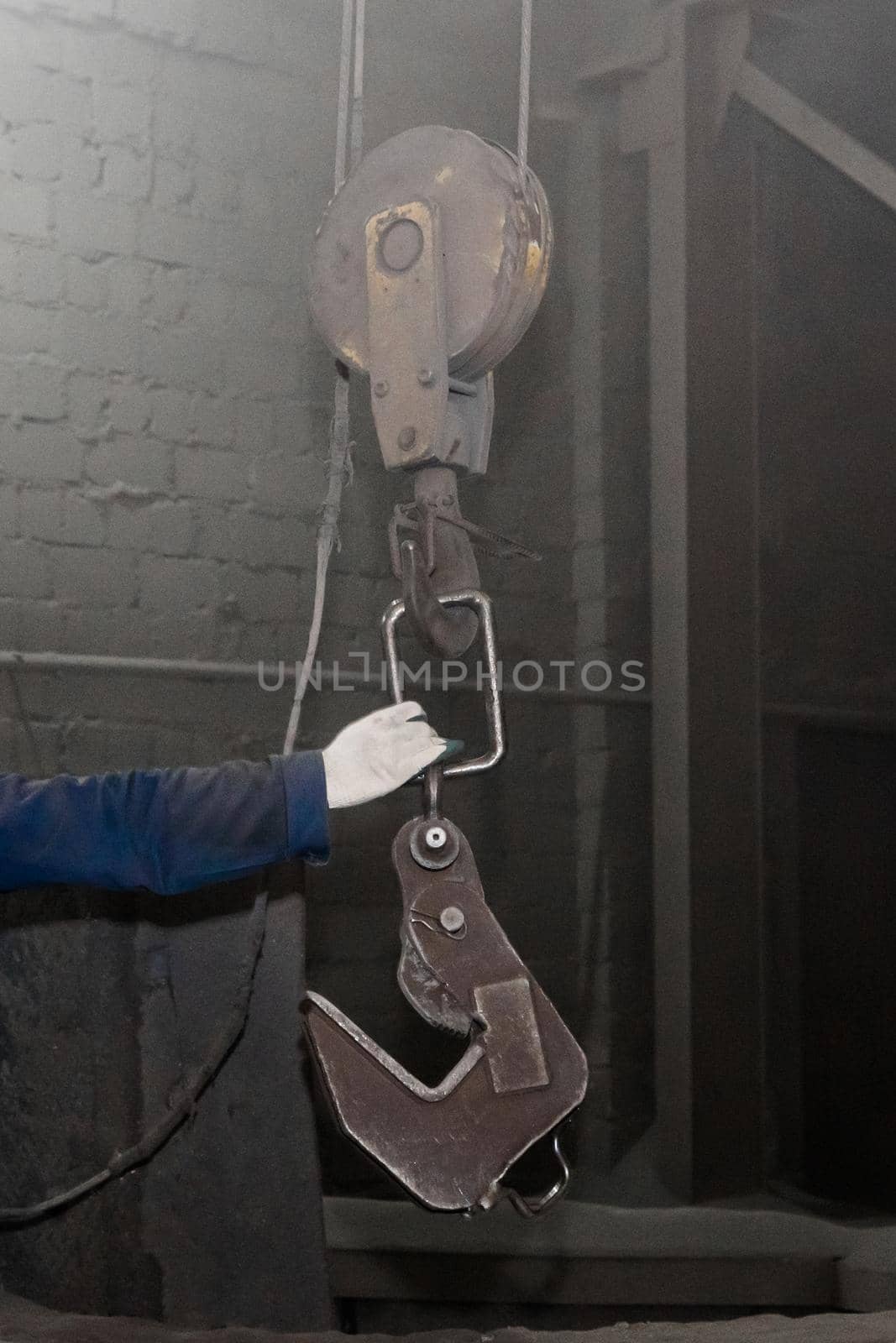 The hand of a working man takes a hook industrial lifting mechanism in the factory workshop.