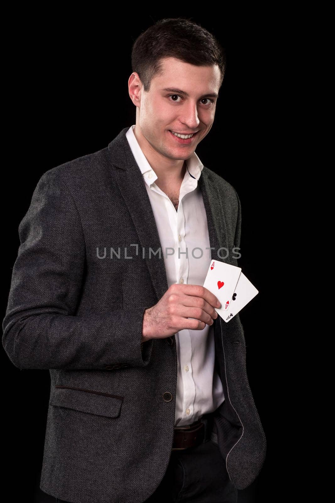 Young caucasian man in a dark suit and a white shirt holding two aces in his hand on black background. Gambling concept. Casino