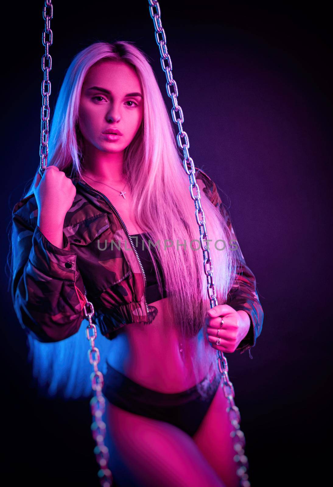 beautiful stylish fashionable girl in bodysuit posing in photo Studio on dark background with chains in neon light by Rotozey
