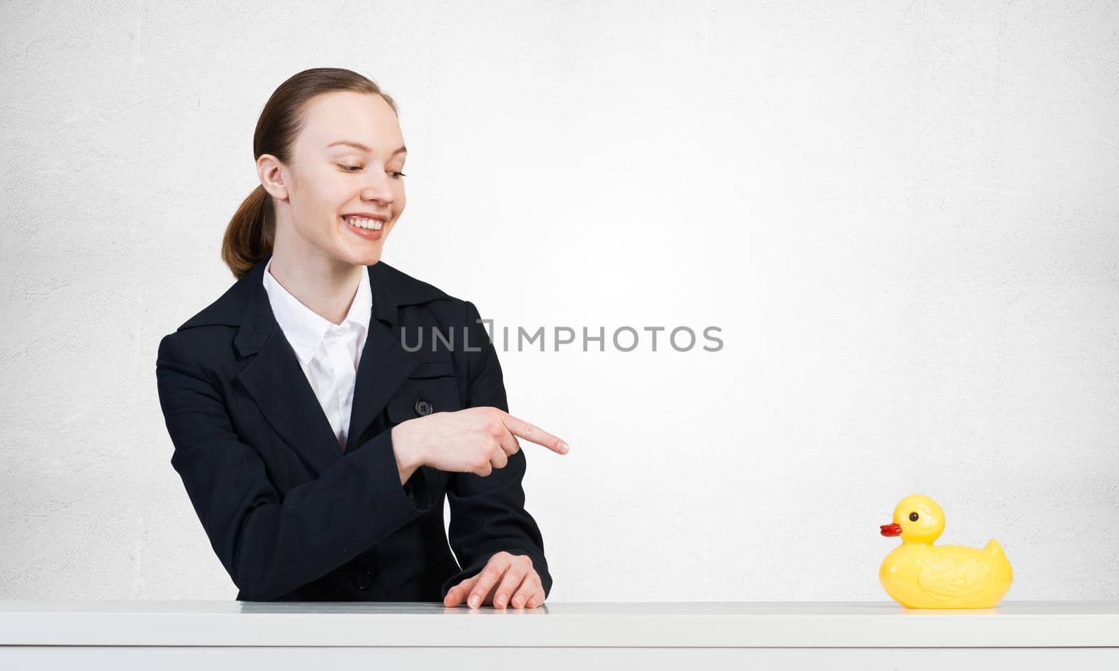 Business woman points her finger at a plastic duck. He sits at the table and smiles.