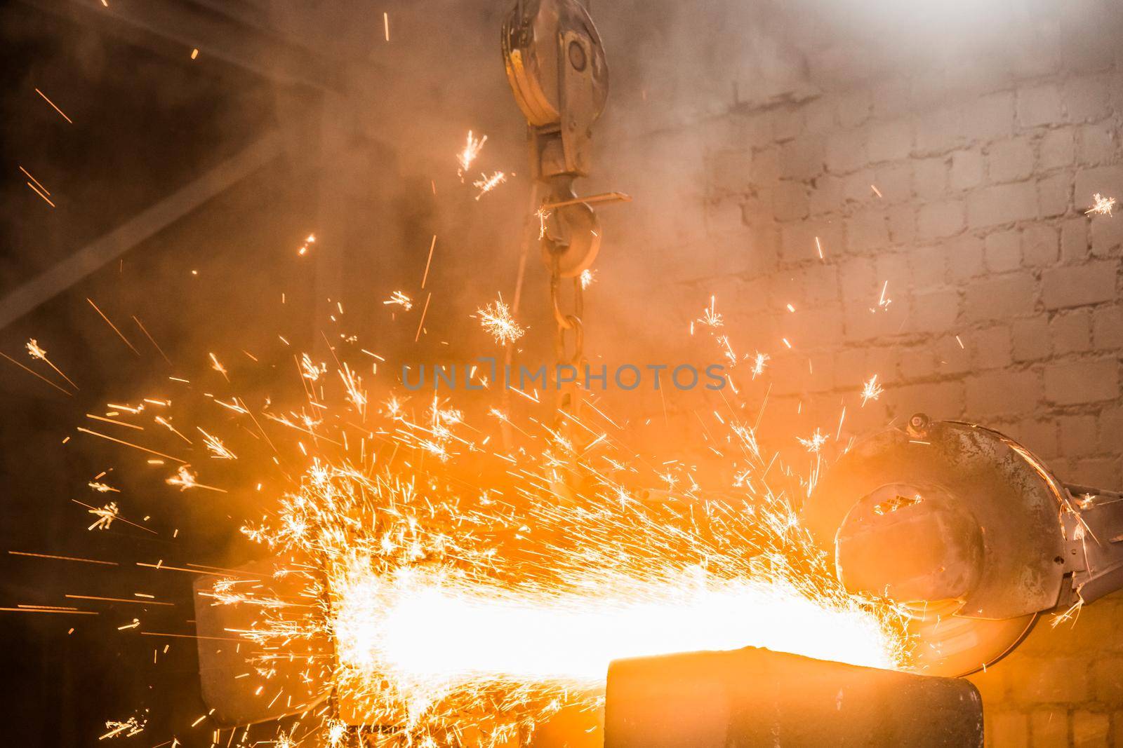 Heavy grinding equipment suspended on a chain with a hook processes and cleans cast iron reinforced concrete tubing in the workshop of an industrial plant.