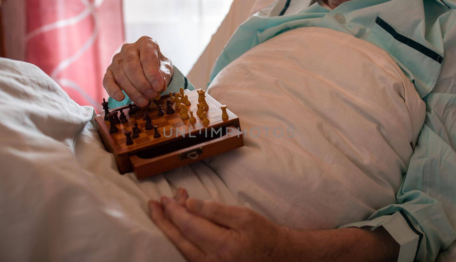 Close up of senior man's hand holding chess board and pieces in lap in medical bed in hospital