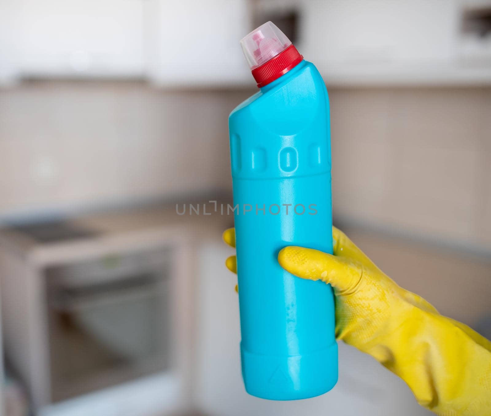 Close up of female hands with protective gloves holding bottle with disinfectant in front of kitchen countertop