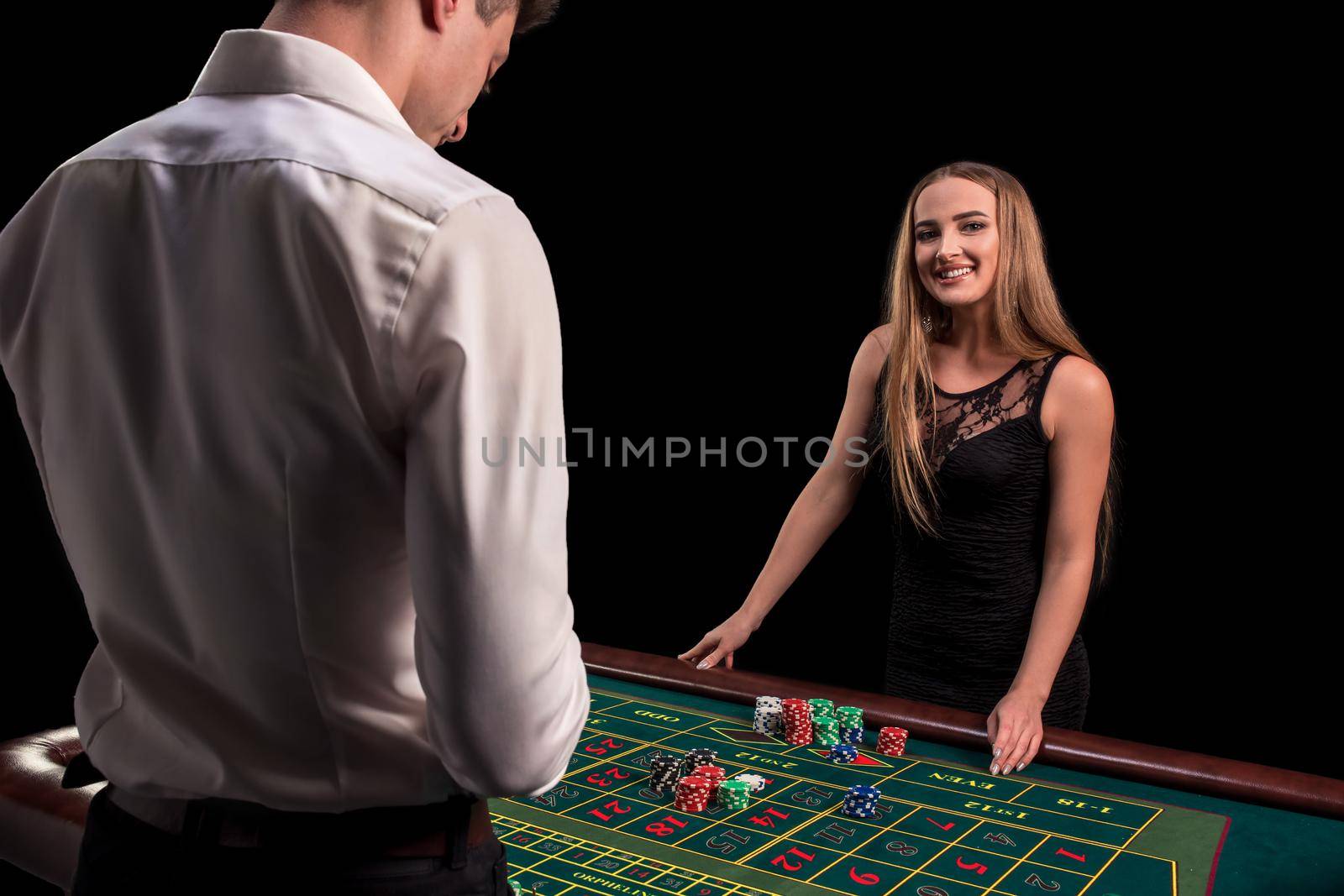 A close-up on the back of the croupier in a white shirt, image of green casino table with roulette and chips, a rich woman betting of gambling in the background. Casino. Gambling. Roulette. Betting