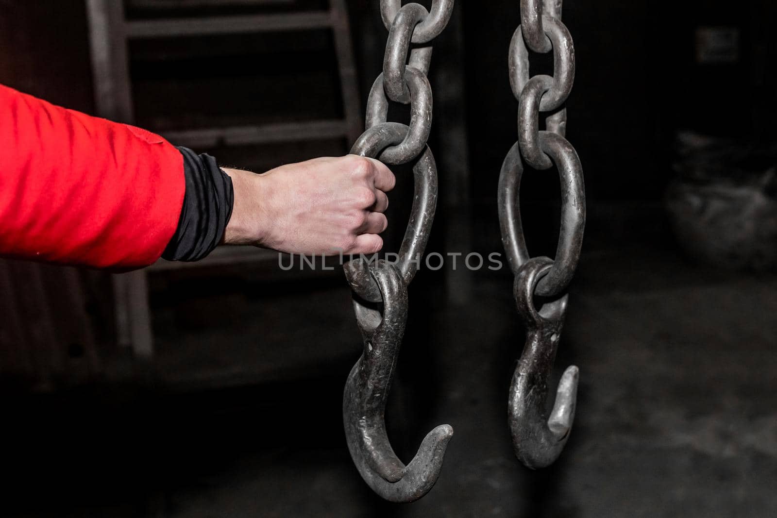 The hand of a male worker holds an iron chain with a hook lifting mechanism of a crane in an industrial plant.