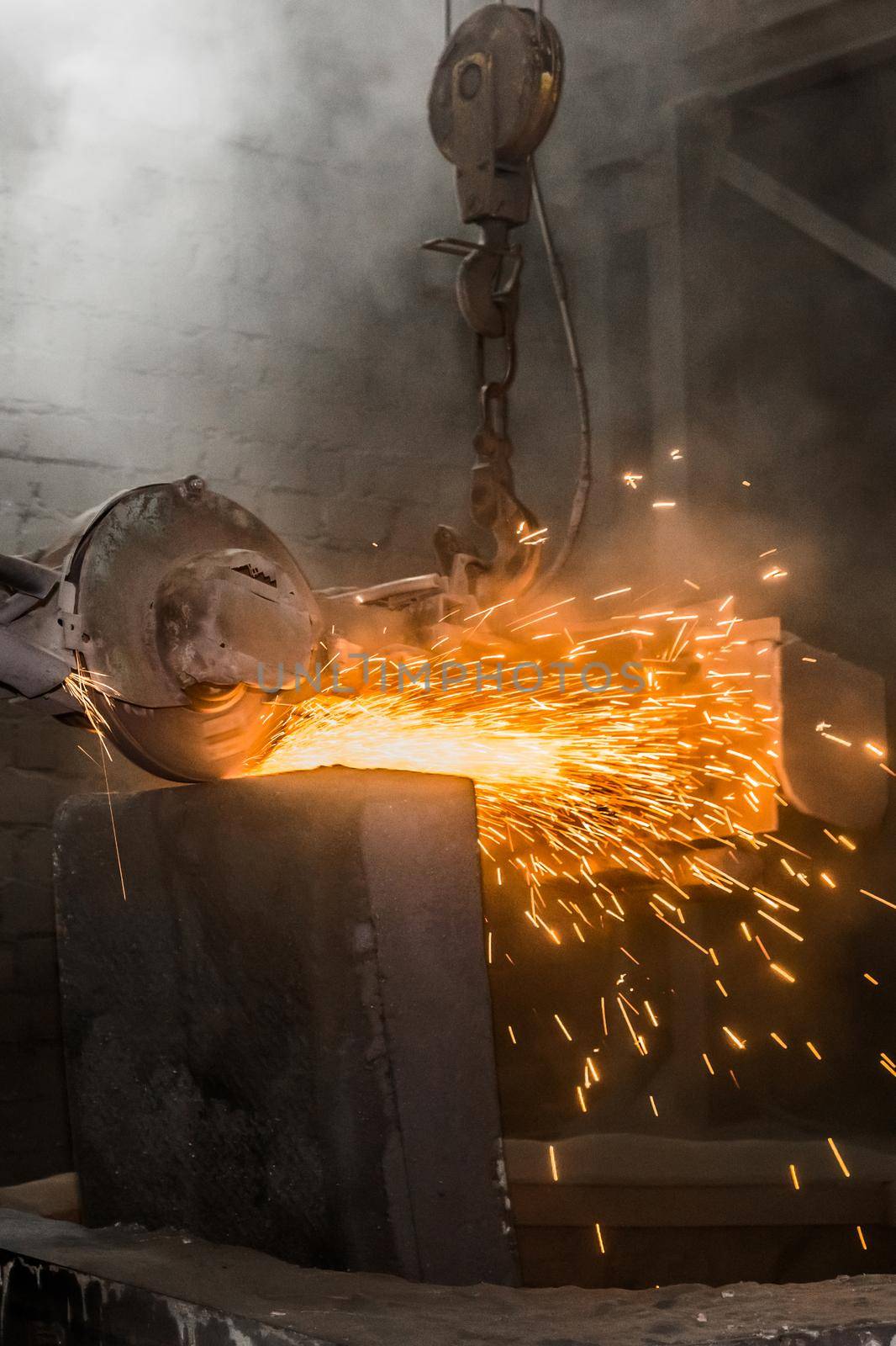 Heavy grinding equipment suspended on a chain with a hook processes and cleans cast iron reinforced concrete tubing in the workshop of an industrial plant.