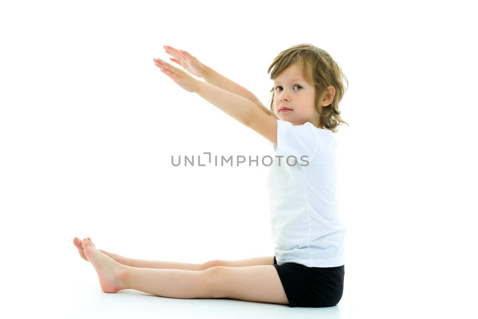 Cute little girl performs gymnastic exercises on the floor in the studio on a white background. The concept of sports, the physical development of children