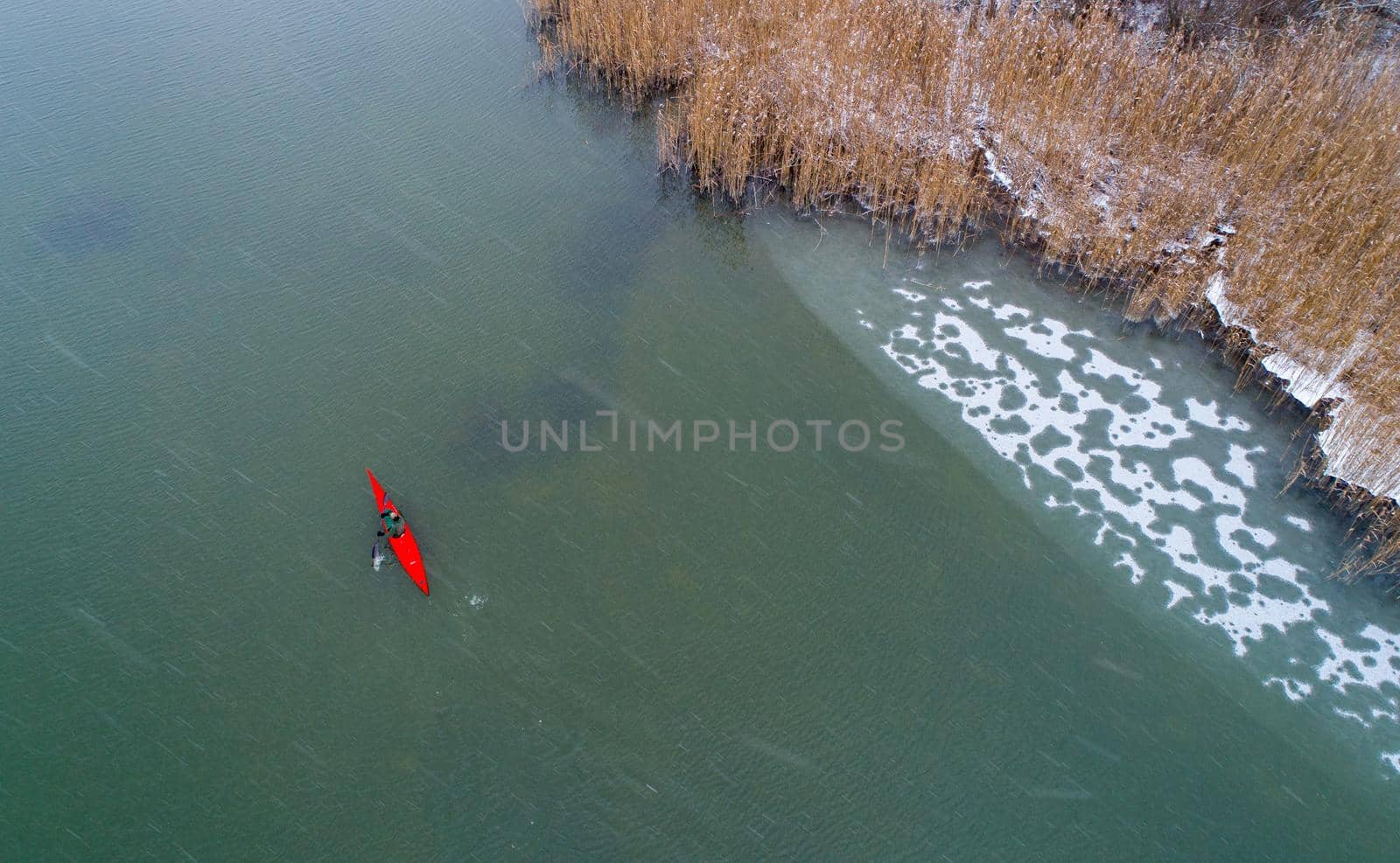 Top view of man in red kayak in cold frozen river on winter day