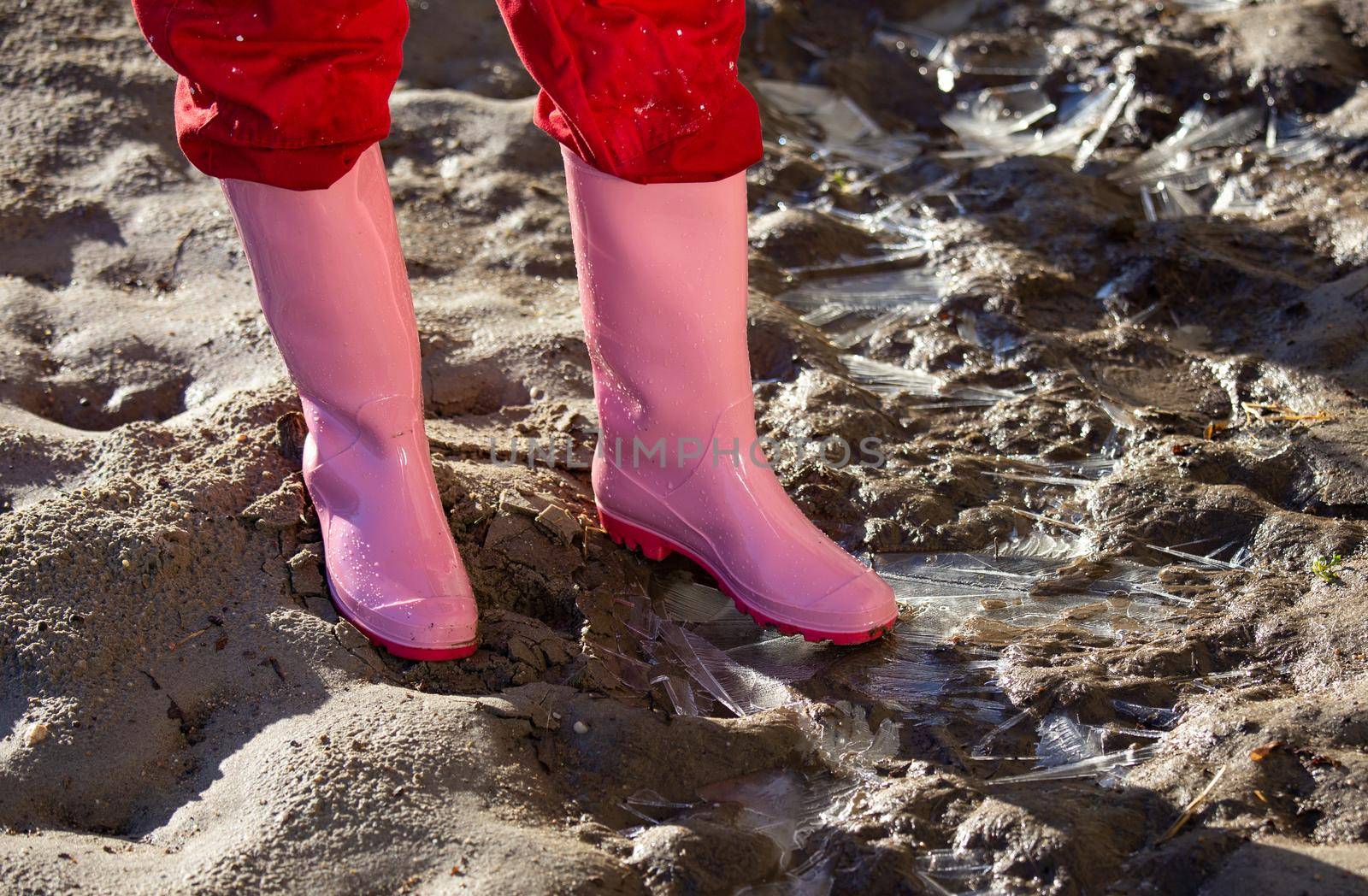 Close up of female legs in pink gumboots standing on frozen sandy ground