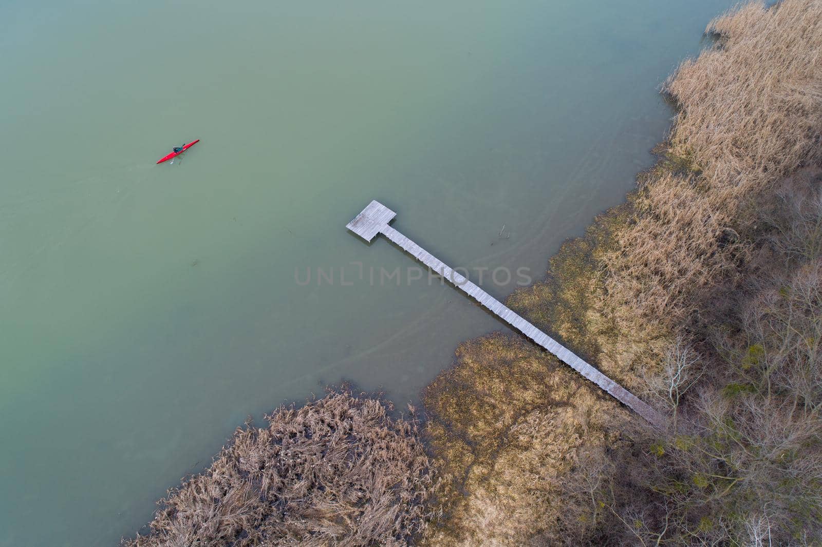 Top view of man in red kayak beside private wooden dock in cold frozen river on winter day