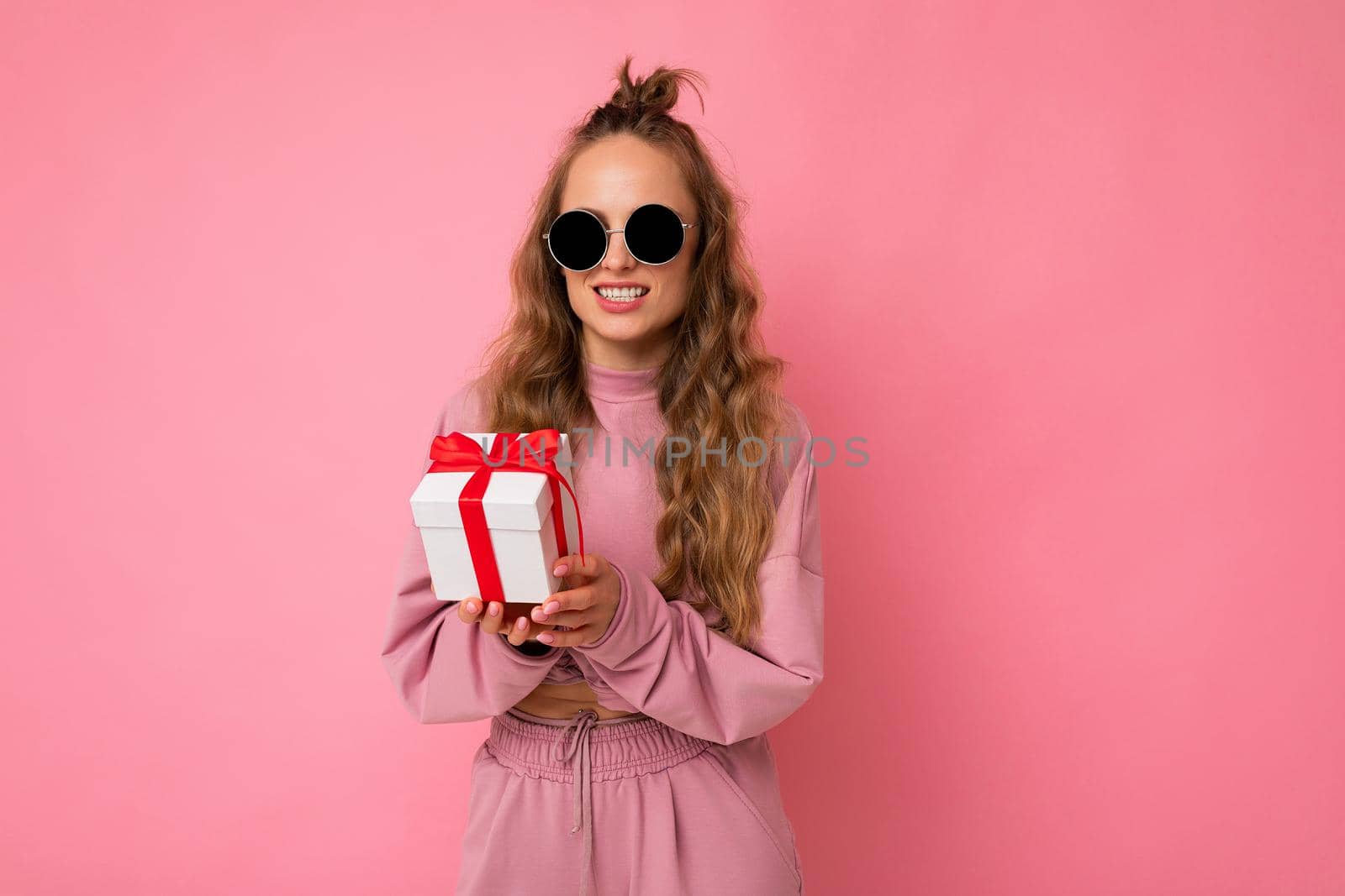 Shot of attractive positive smiling young blonde woman isolated over colourful background wall wearing everyday trendy outfit holding gift box and looking at camera.