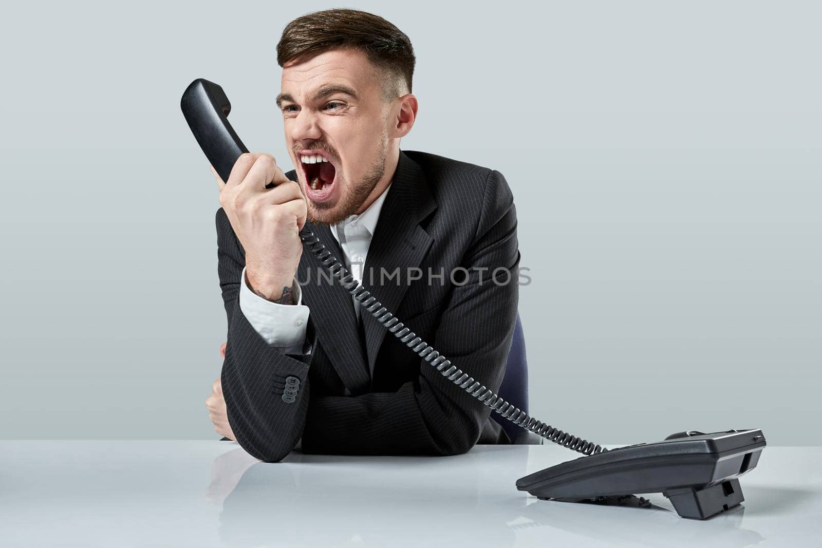 A young man in a black suit dials the phone number while sitting in the office. Manager talking on the phone. Man emotionally shouts