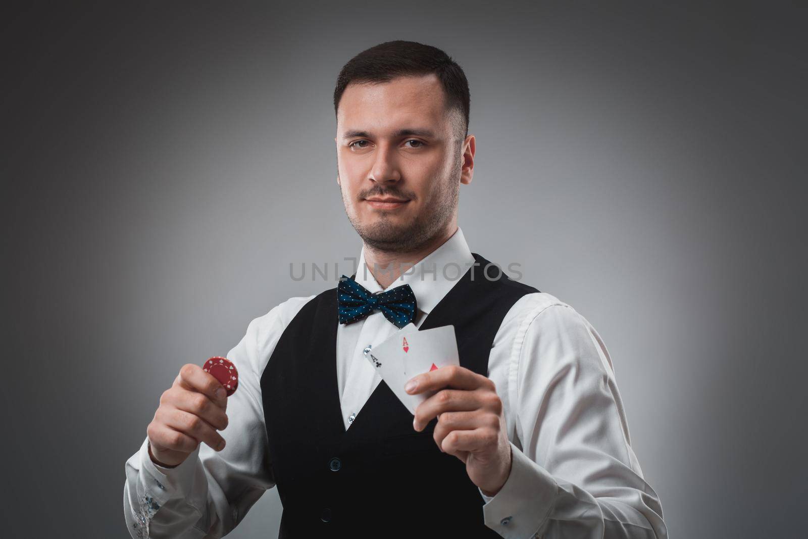 Young man in shirt and waistcoat shows his cards and holds poker chips in his hands, studio shot. Poker. Emotions