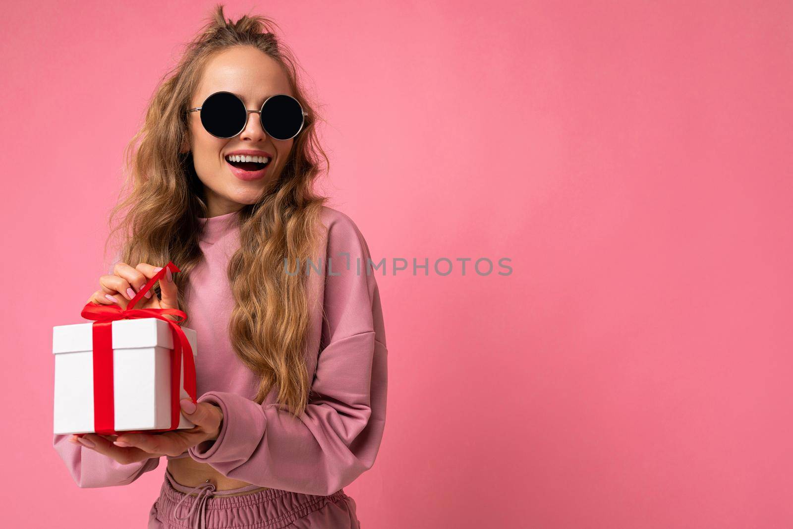 Beautiful happy young brunette woman isolated over colourful background wall wearing stylish casual clothes holding gift box and looking to the side. Empty space