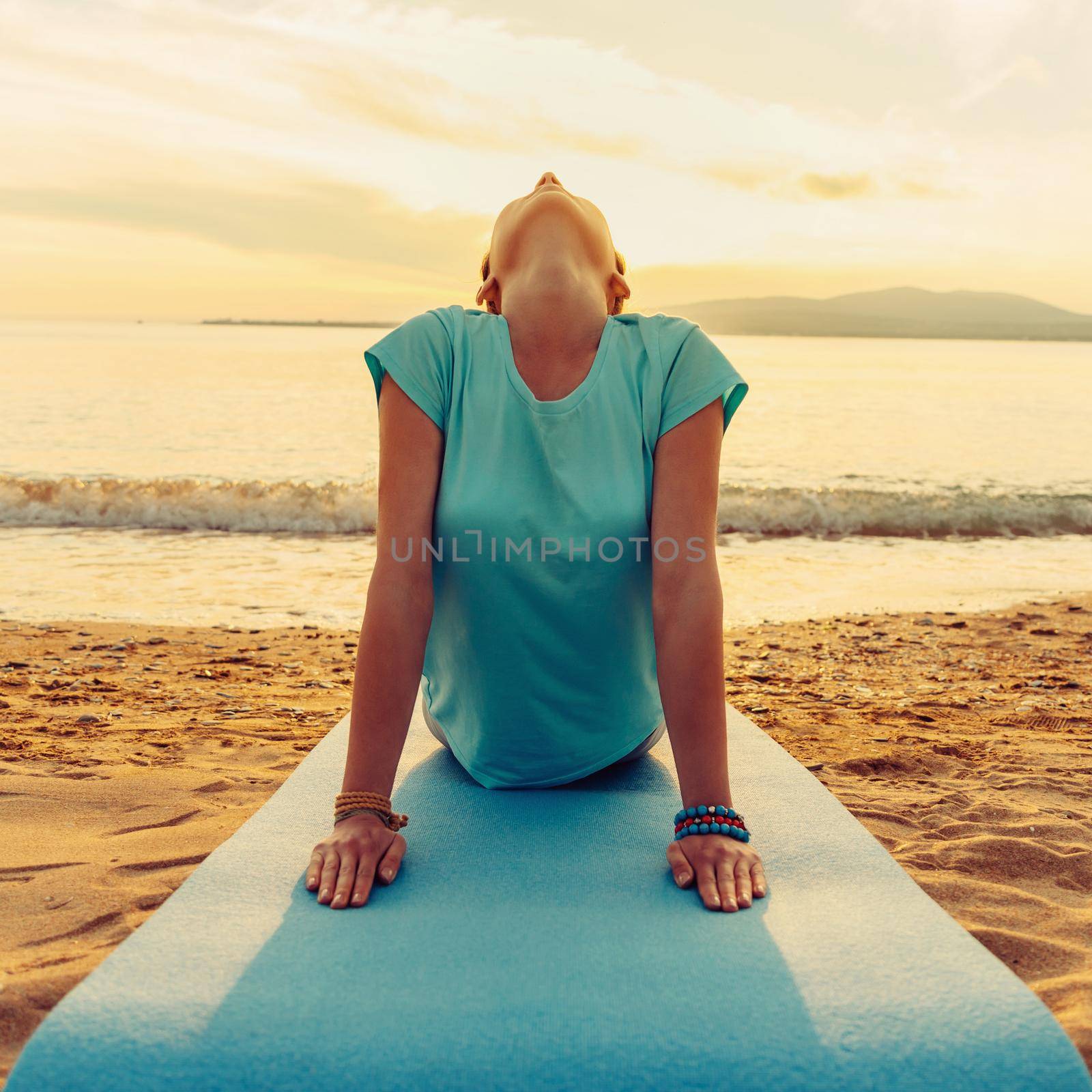 Young woman practicing yoga in upward facing dog pose on beach near the sea on sunset, front view