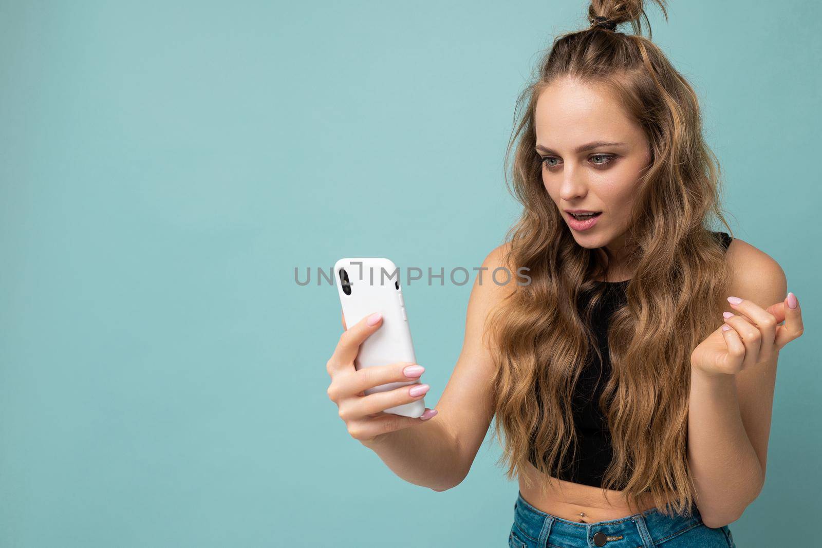 Beautiful young woman wearing casual clothes standing isolated over background surfing on the internet via phone looking at mobile screen.