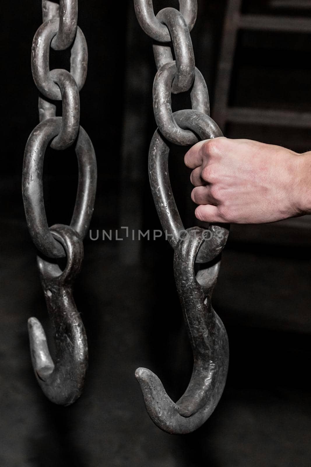 The hand of a man worker holds an iron chain with a hook lifting mechanism of a crane in an industrial plant.