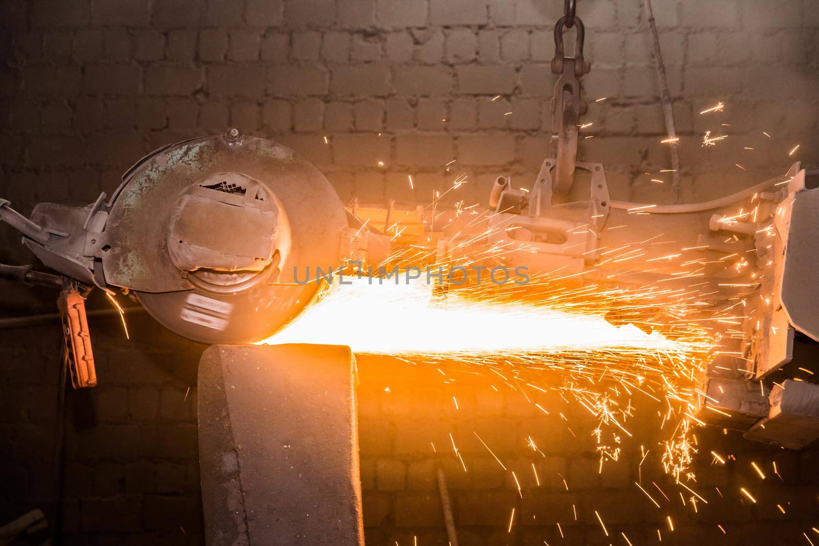 Heavy grinding equipment suspended on a chain with a hook processes and cleans cast iron reinforced concrete tubing in the workshop of an industrial plant by AYDO8