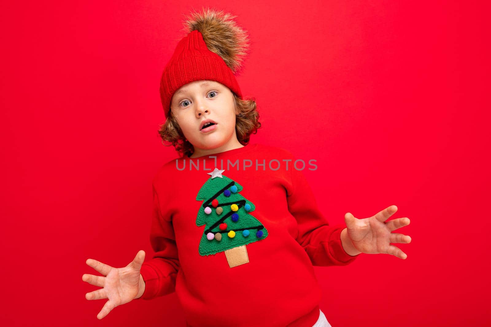 cool boy with curls on a red background in a sweater with a christmas tree.